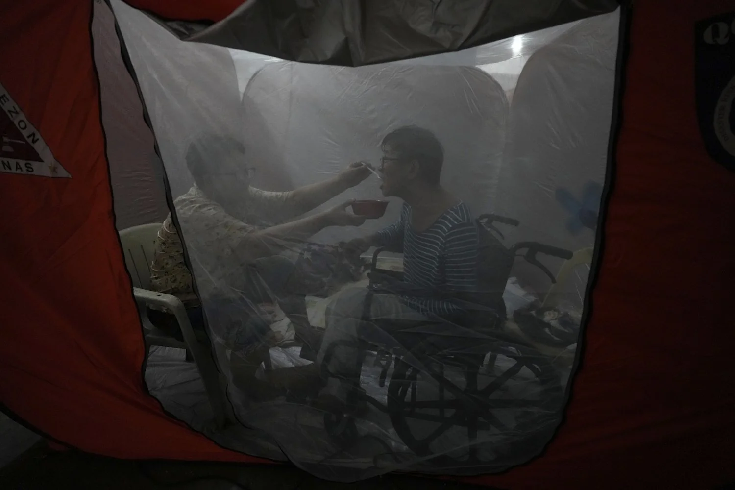  Judy Bertuso, left, feeds her husband Apollo inside a tent at an evacuation center as Typhoon Fung-wong enters the country on Sunday, Nov. 9, 2025 in Quezon city, Philippines. (AP Photo/Aaron Favila) 