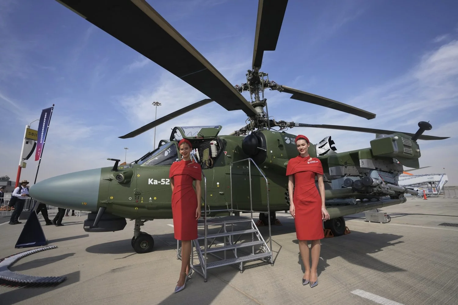  Russian hostesses stand by a Russian KA-52 attack helicopter at the Dubai Air Show in Dubai, United Arab Emirates, Monday, Nov. 17, 2025. (AP Photo/ Fatima Shbair) 