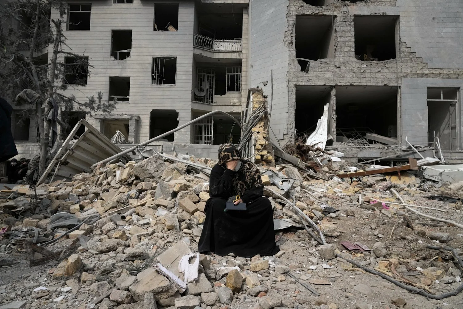  A woman sits on rubble across from a residential building damaged during the U.S.-Israeli air campaign in Tehran, Iran, March 12, 2026. (AP Photo/Vahid Salemi) 