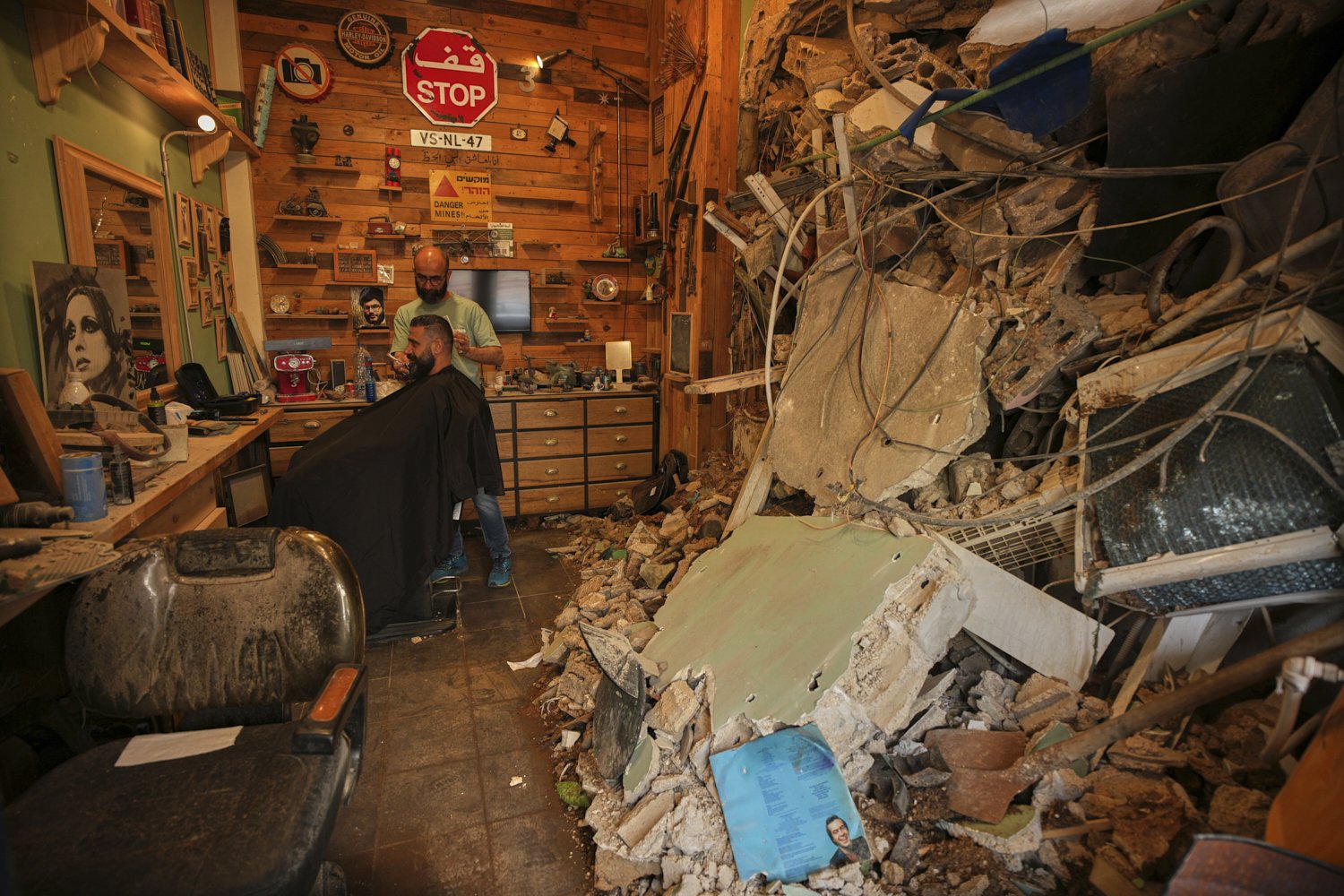  Barber Mohammad Mehdi tends to his client Ayman Al Zein inside his shop that was damaged in an Israeli airstrike in Dahiyeh, Lebanon, April 18, 2026. (AP Photo/Hassan Ammar) 