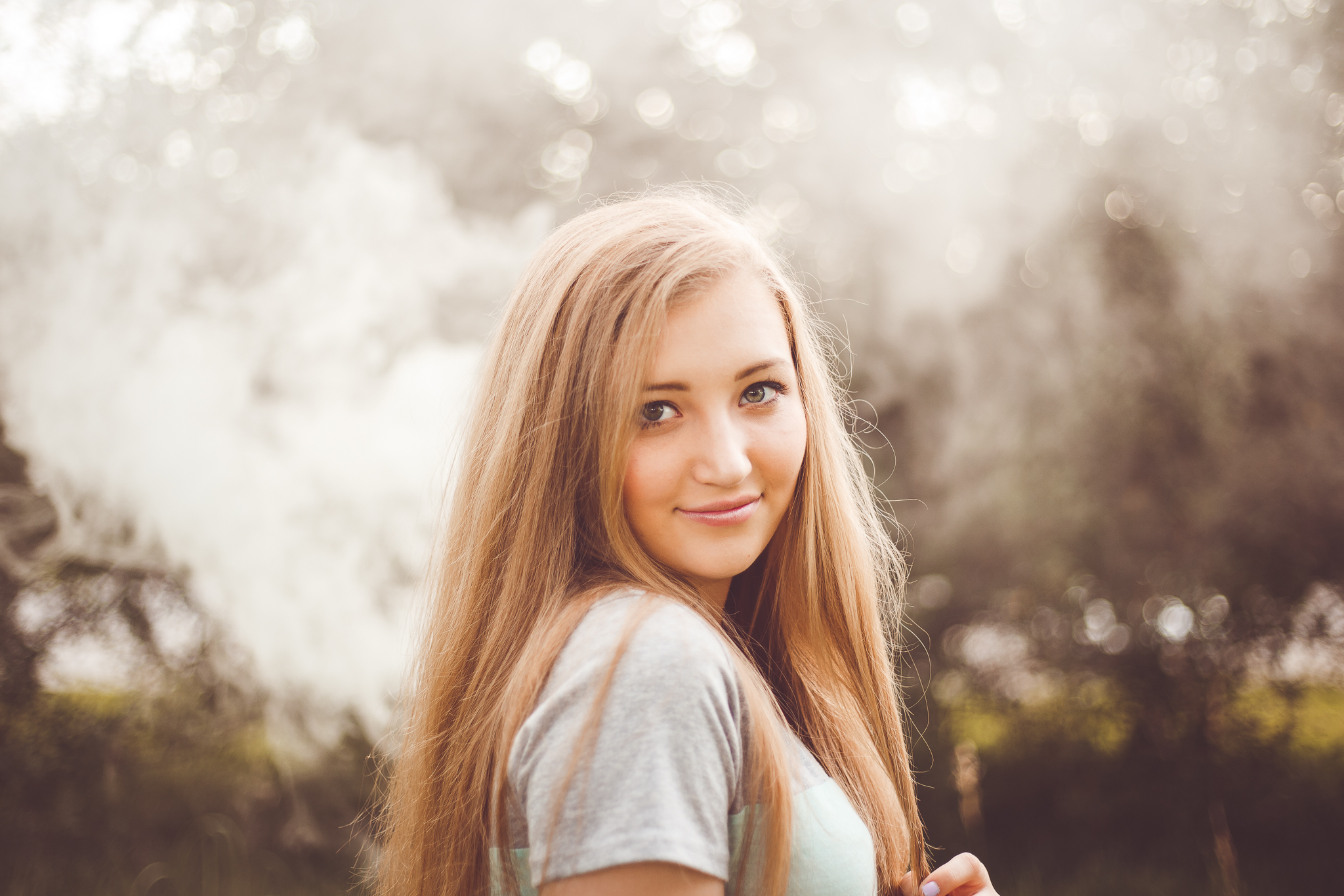 A beautiful senior girl with long blonde hair smiles at the camera with the golden sunset behind her in this outdoor senior photography session by L+R Photography from Tulsa, OK