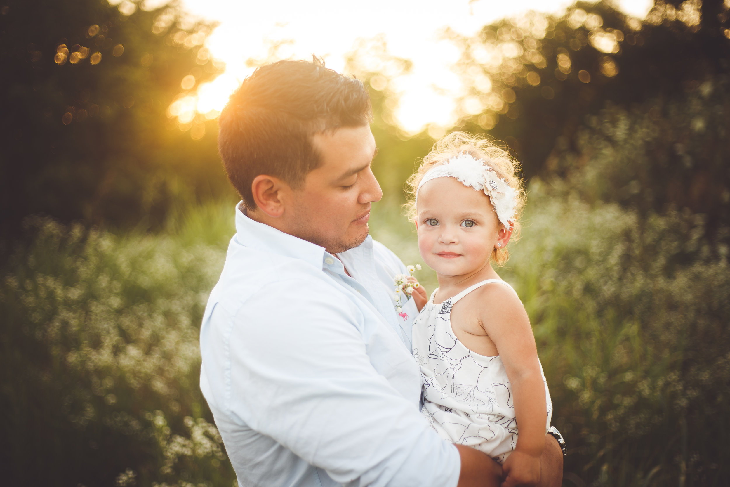 A younf father holds his beautiful young daughter wearing a white headband in his arms