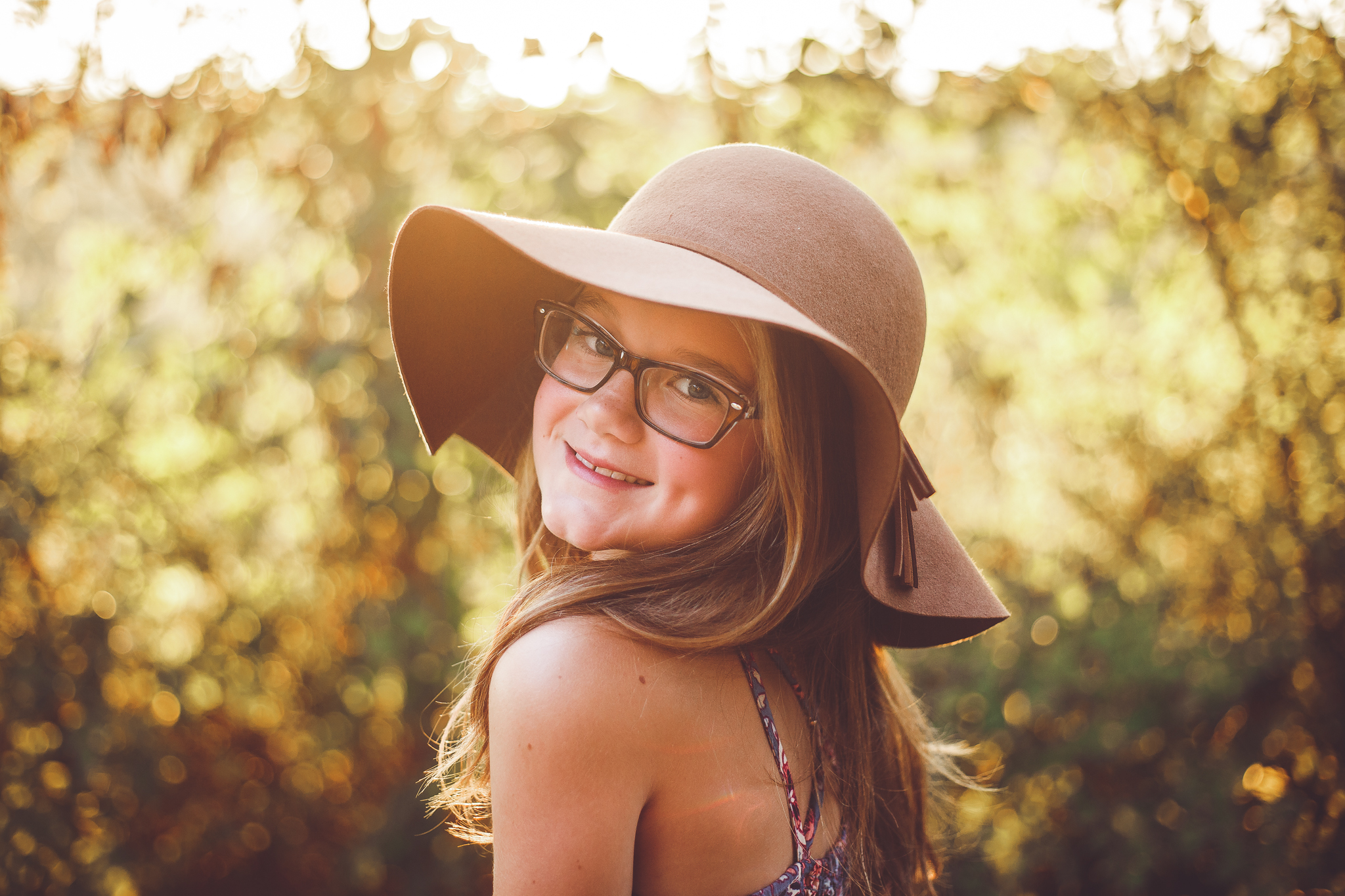 A very cute young girl looks back at the camera and smiles and dimples, wearing a hat in this child photography by L+R Photography from Tulsa , Oklahoma