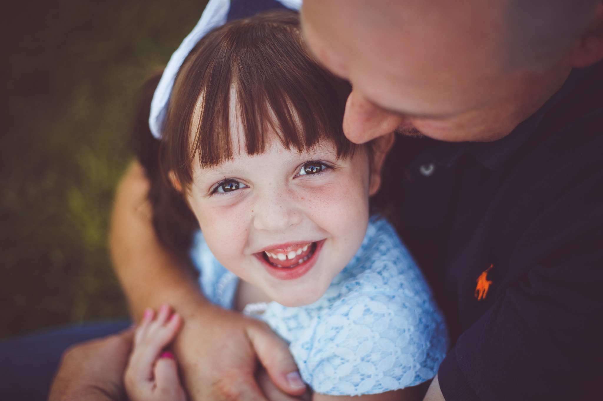 A father holds his daughter in his arms as she looks up and smiles big for the camera - Child Photographer - L+R Photography - Tulsa, Oklahoma