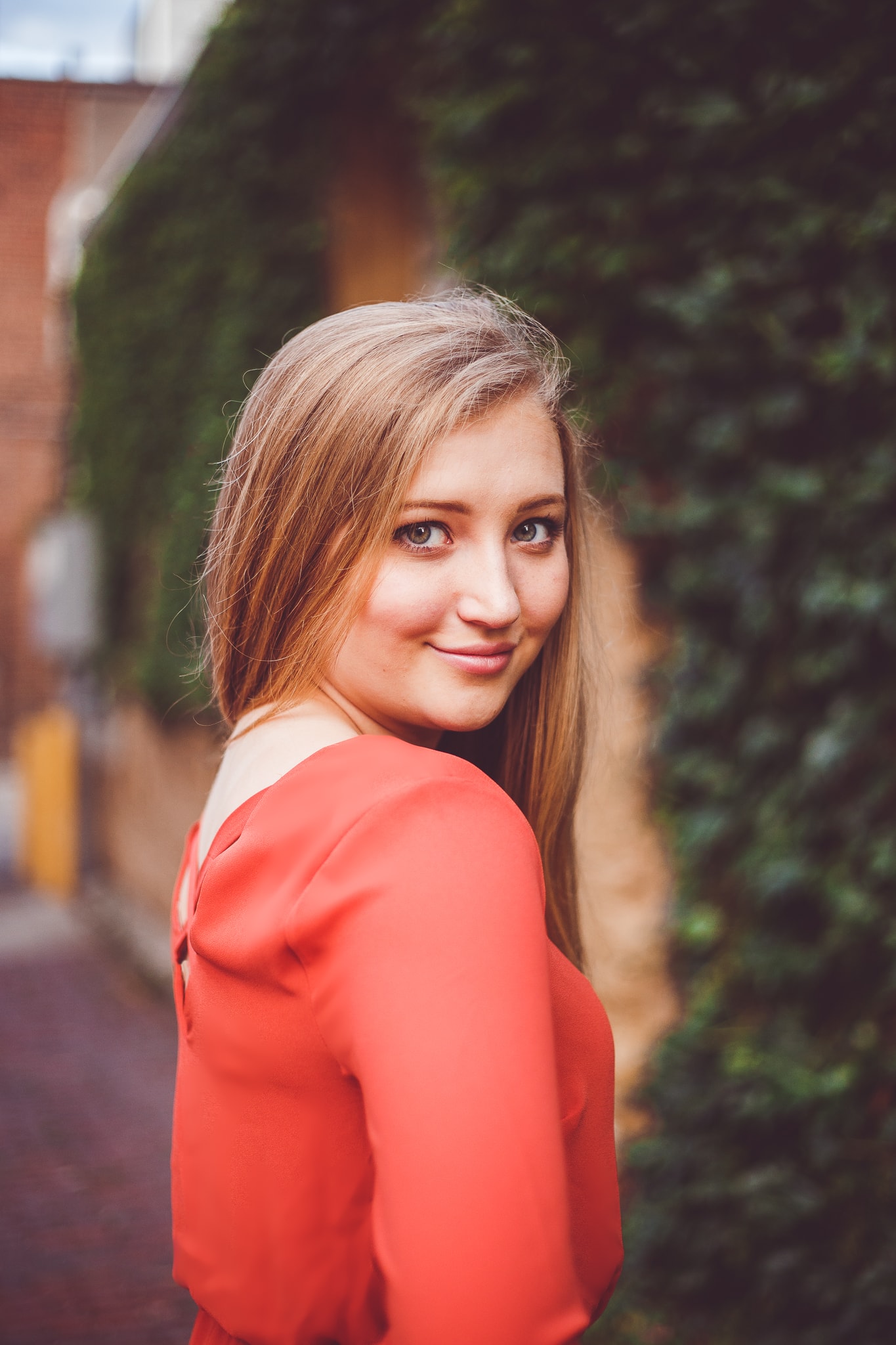 A beautiful young high school senior girl wearing an red toop, stands sideways to the camer and looks back in this outdoor, natura light senior photograph by L+R Photography in Tulsa, OK