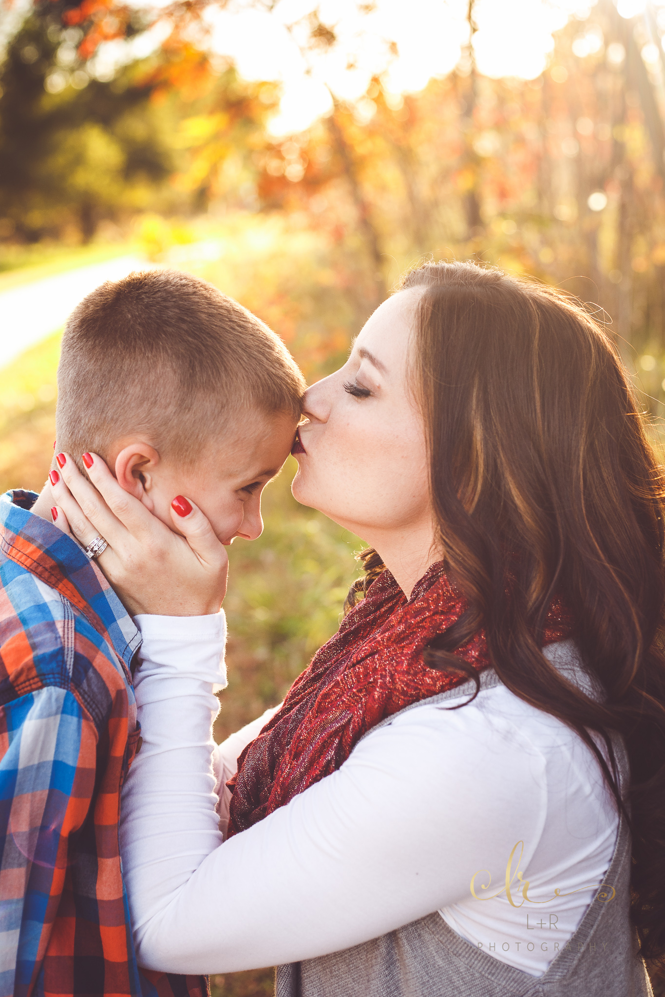 A young mother wearing a striking red scarp tenderly kisses the forehead of her son in this family photograph by L&R Photography of Tulsa, OK