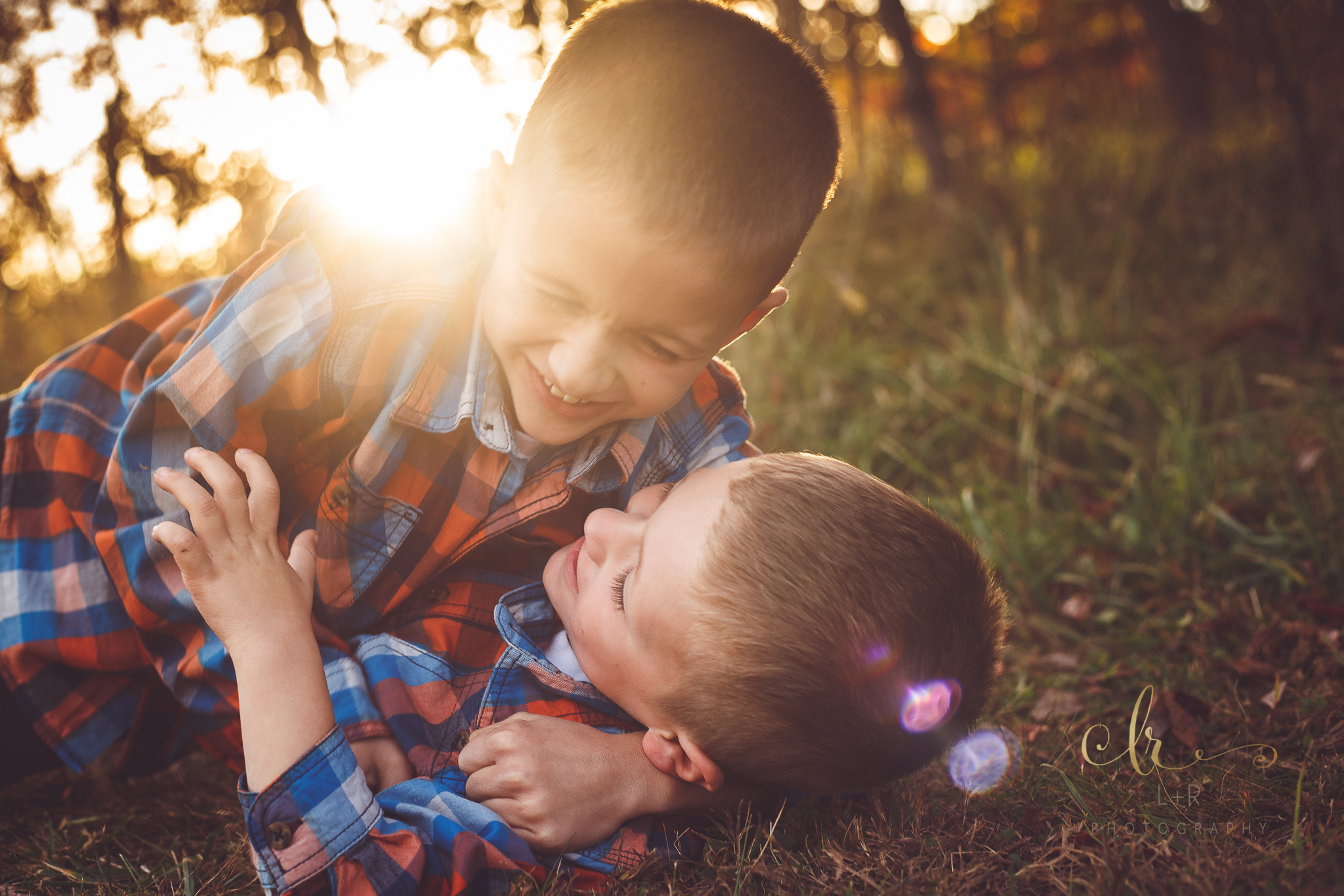 Two young brothers enjoy a moment, wrestling on the ground and laughing during this sunset family photography session by L&R Photography