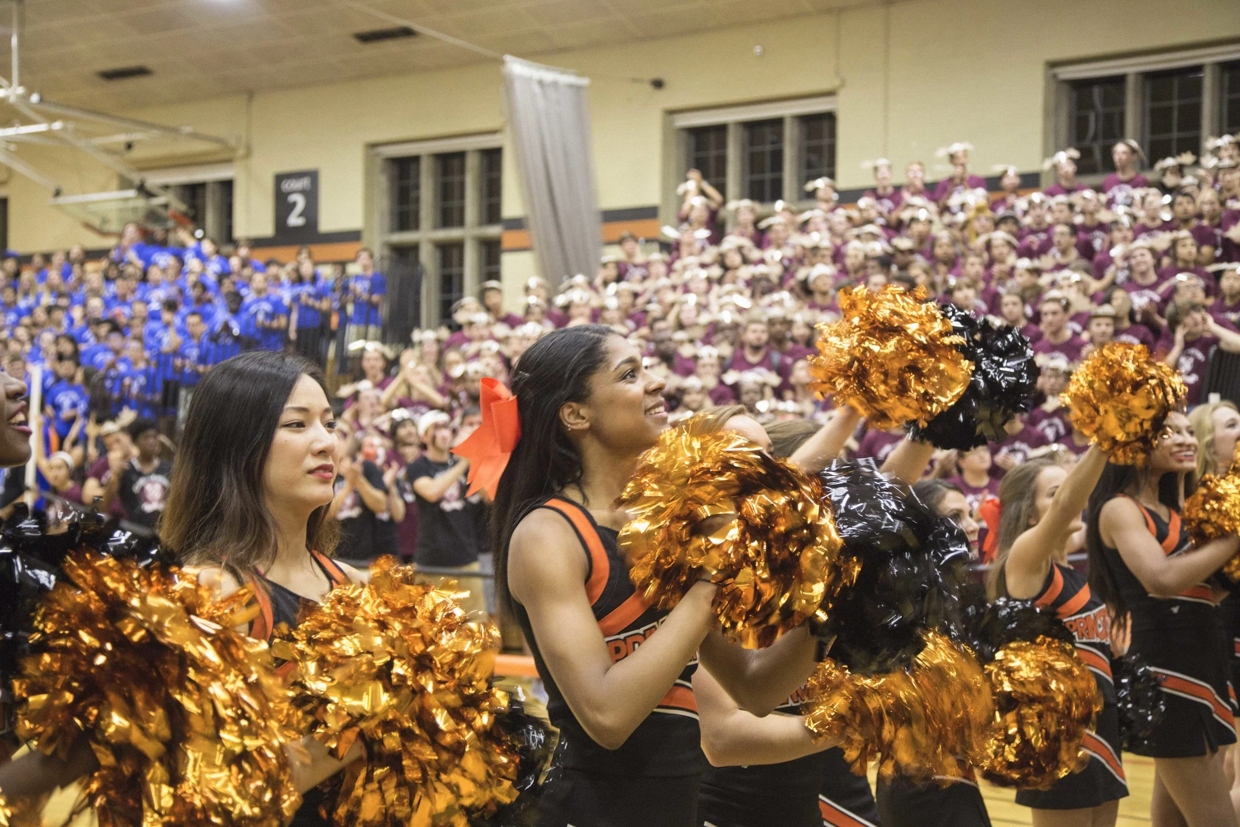 Several women cheerleader students at a University sports game in an indoor gymnasium.