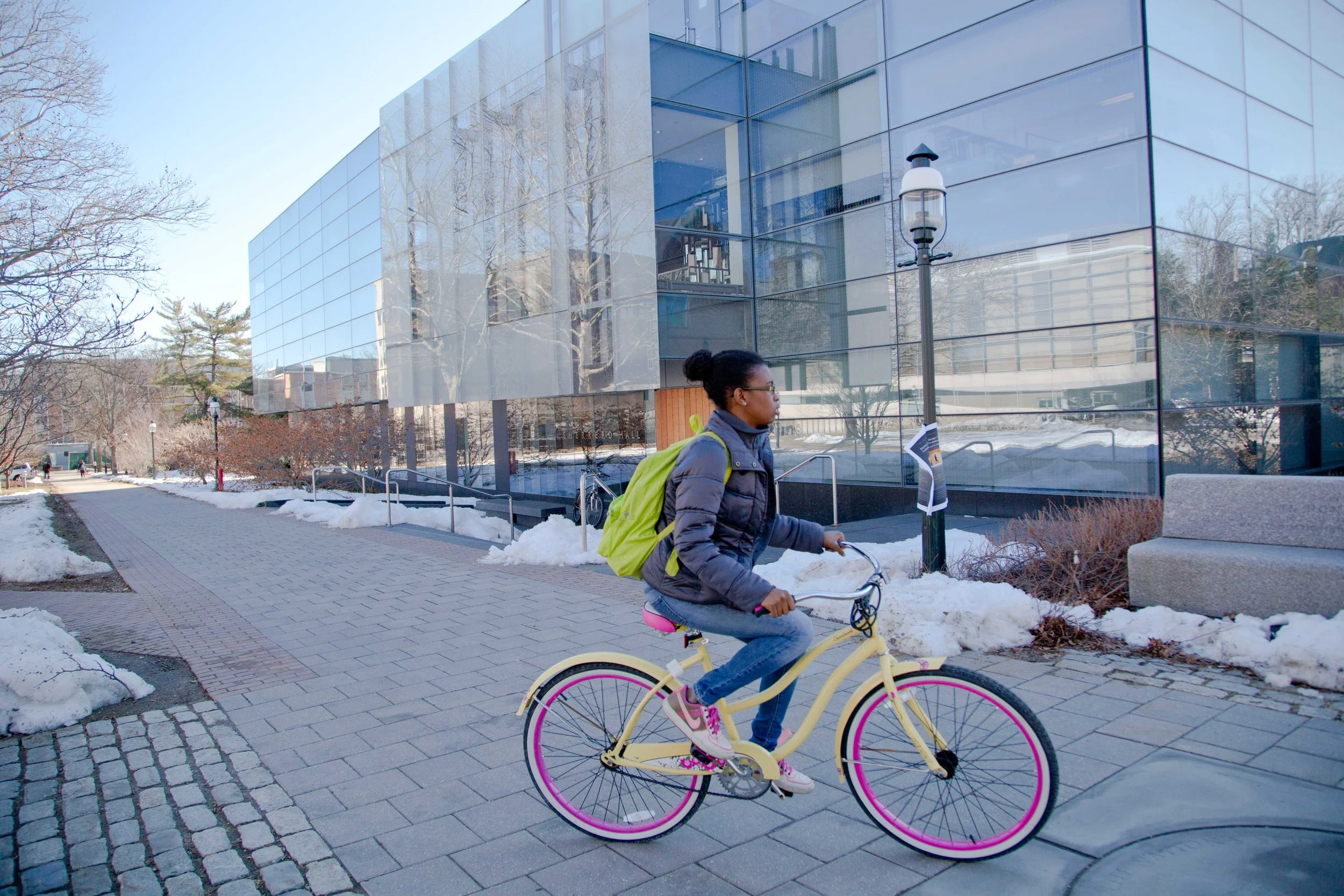 An African American woman student rides a colorful bike on a snowy Princeton campus.