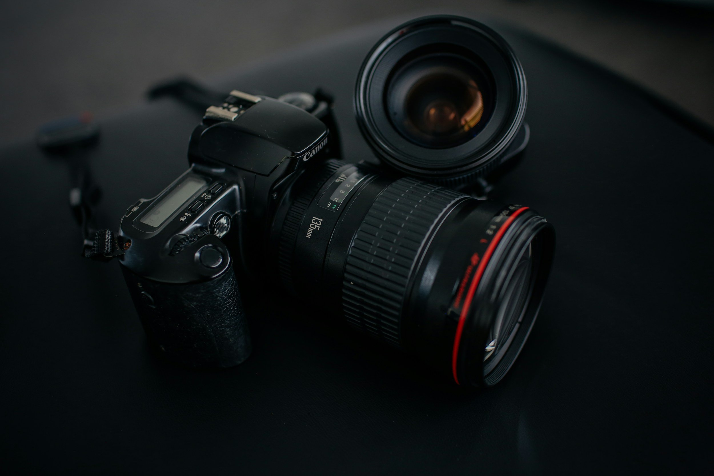 A professional Canon camera with a large zoom lens placed on a dark surface.
