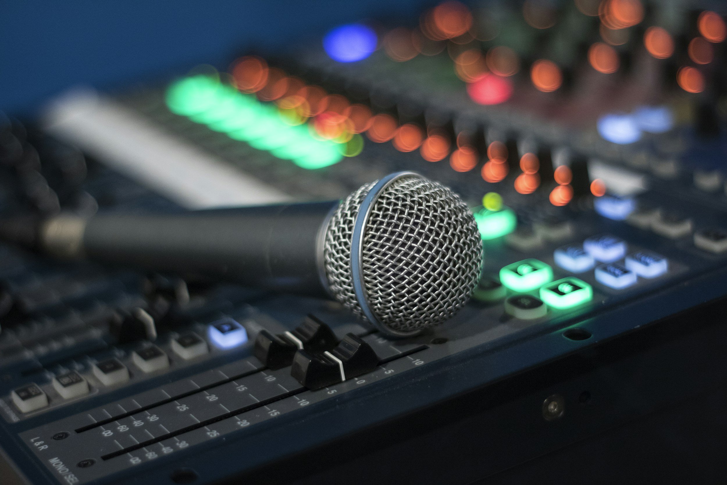 A microphone resting on a sound mixing console with colorful, blurred lighting in the background.