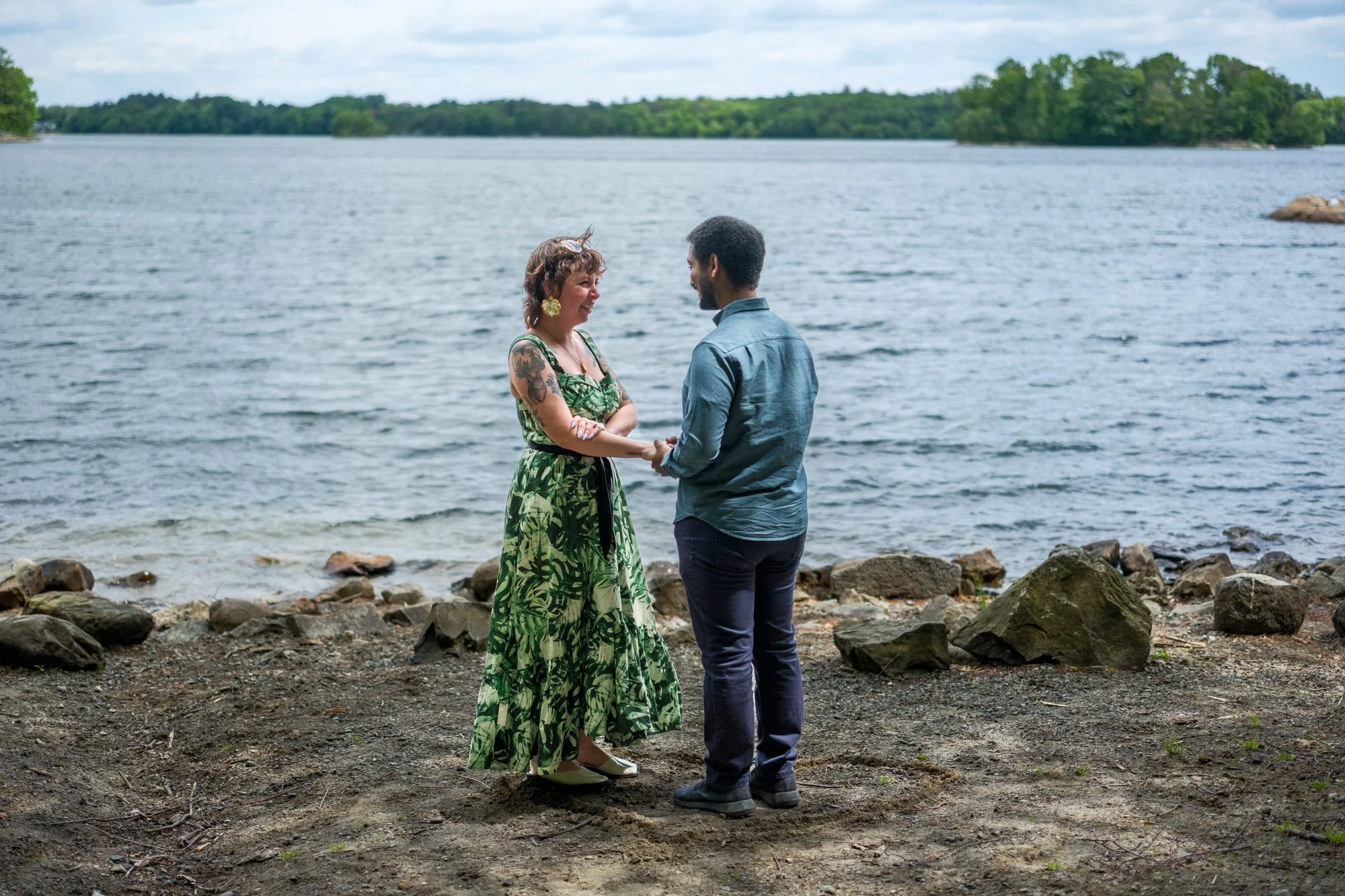 Couple standing together by the water before a spring proposal at Middlesex Fells Reservation