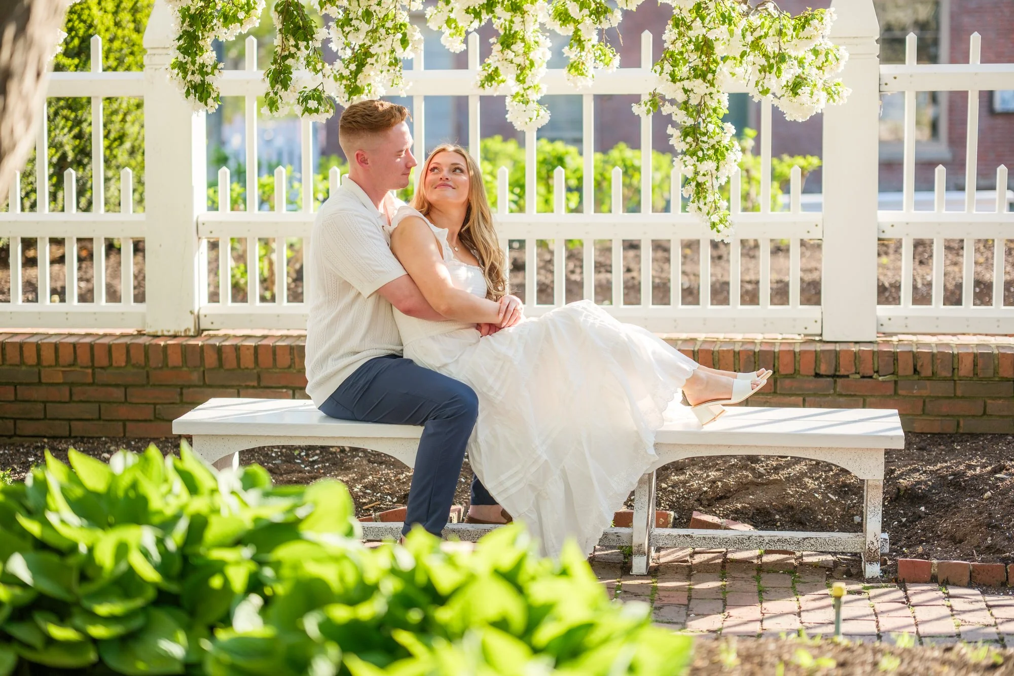 Melanie and Connor walk down vibrant red brick stairs between historic brick buildings, smiling at each other during their engagement session in Portsmouth, NH