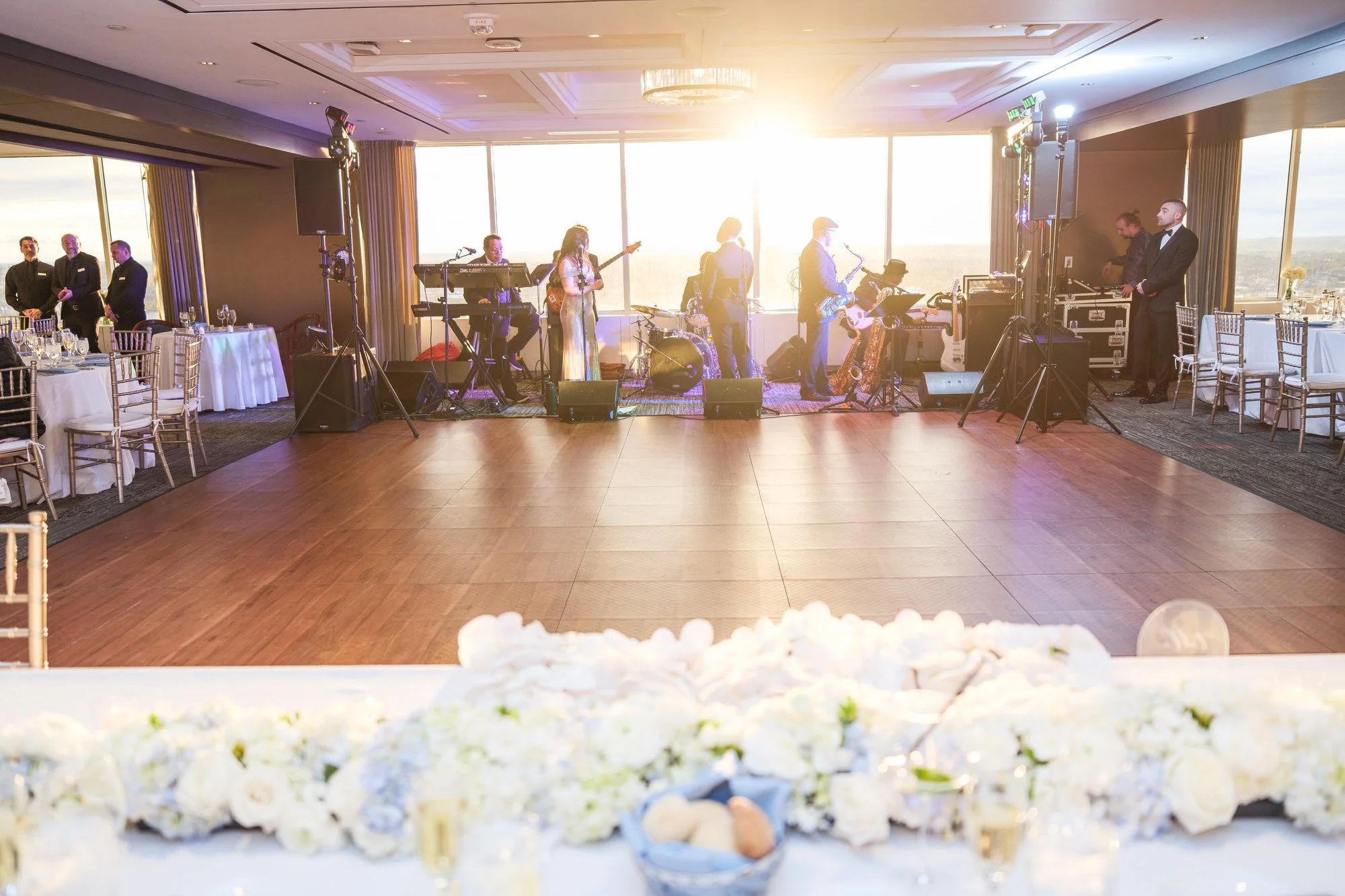 Live wedding band performing on stage with empty dance floor at the UMass Club Boston reception during sunset