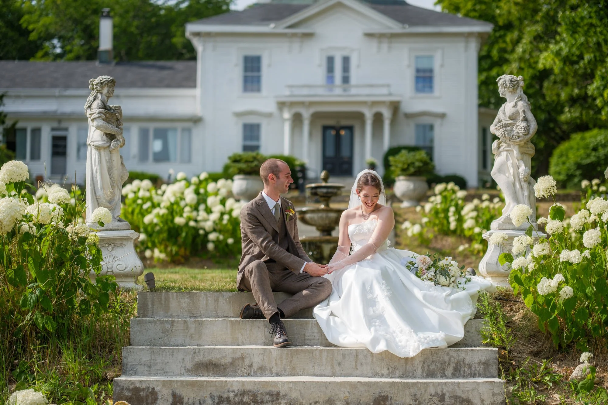 Bride and groom seated on stone steps among white hydrangeas