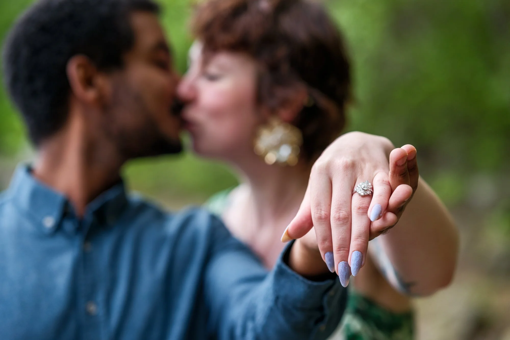 Engagement ring close-up with couple kissing softly in the background