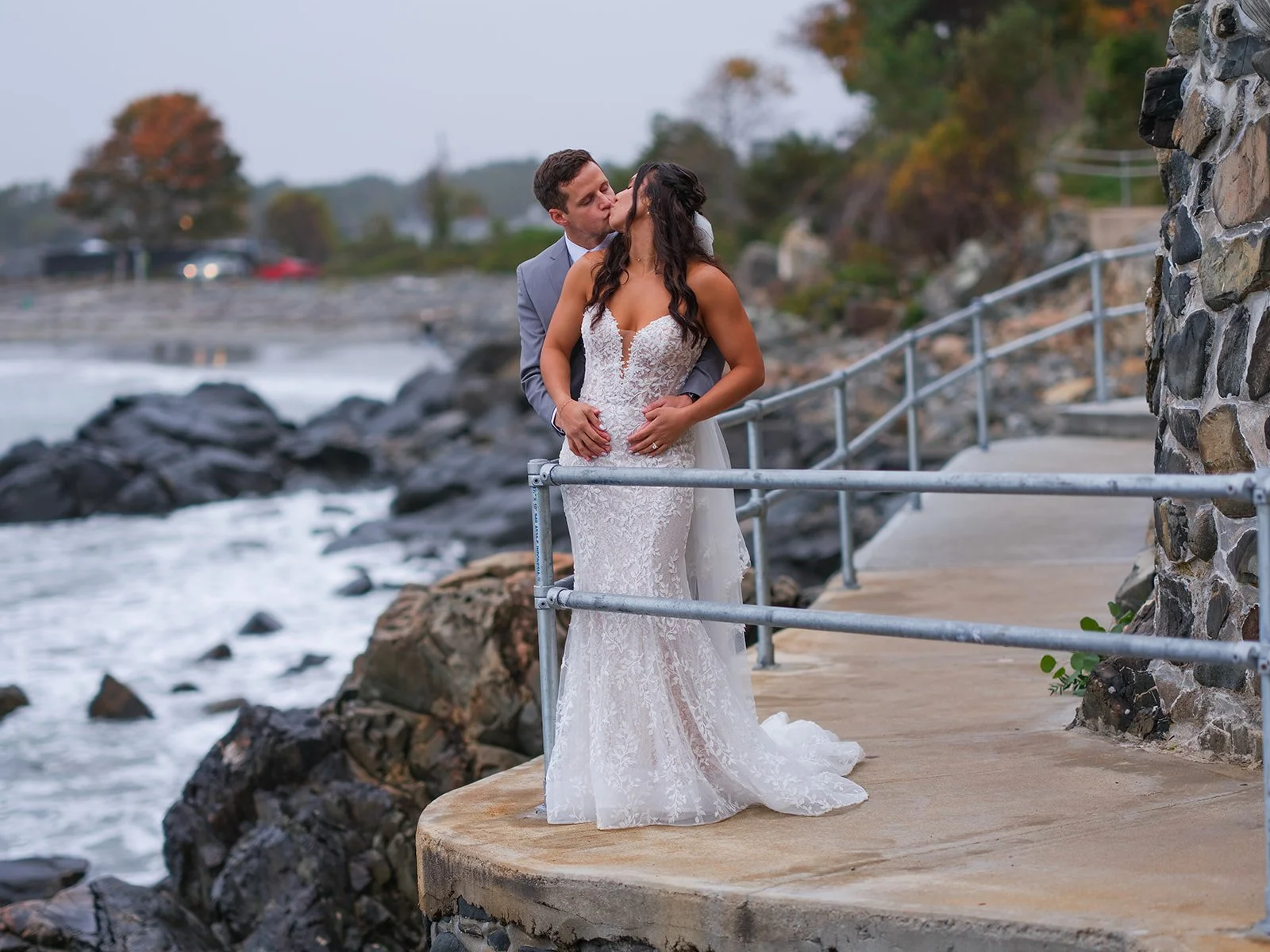 Bride and groom kissing on a rocky seawall with crashing Atlantic Ocean waves behind them in York Maine