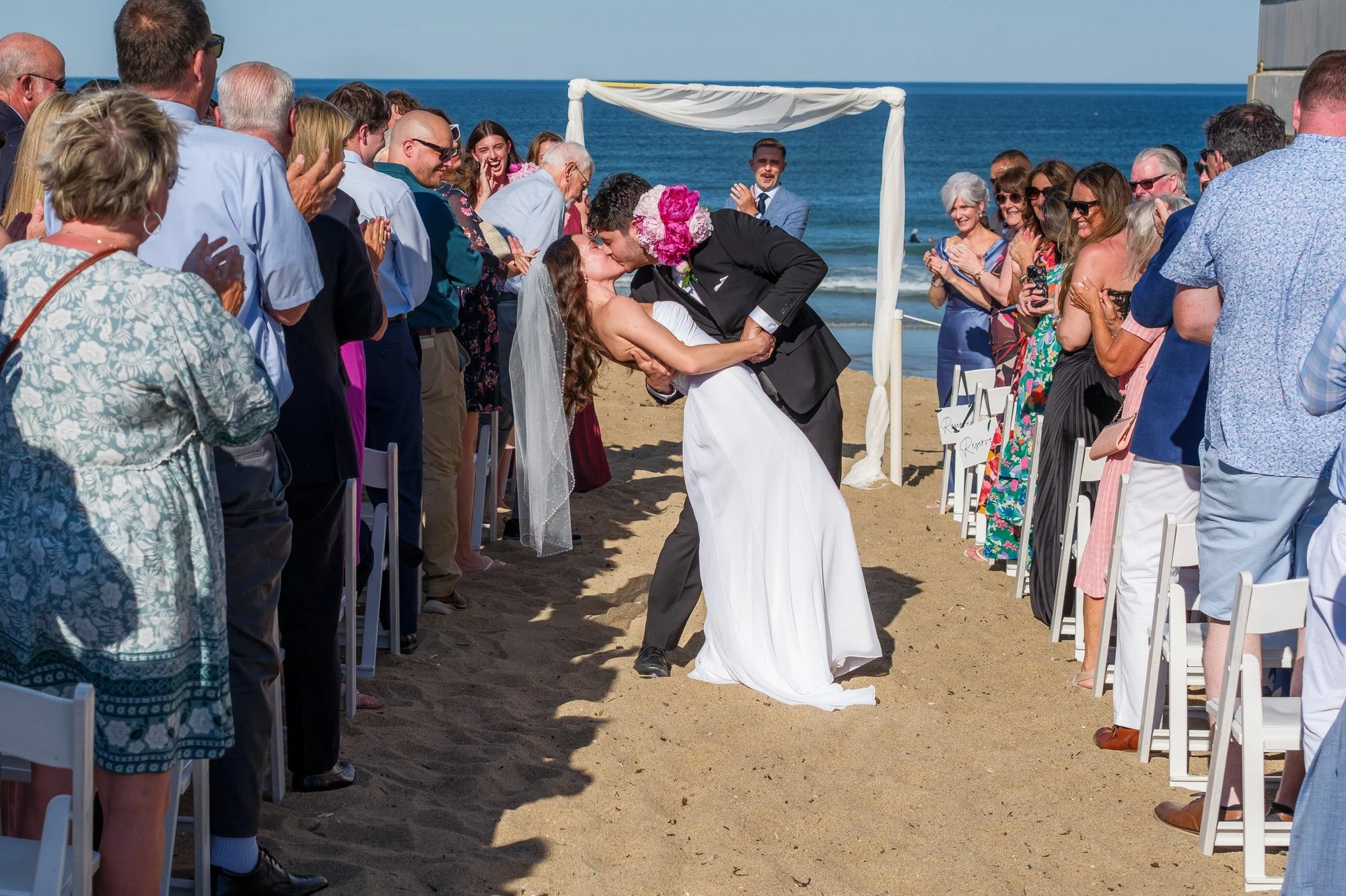 Newlyweds kissing as guests applaud at their oceanfront wedding ceremony in Salisbury, MA.