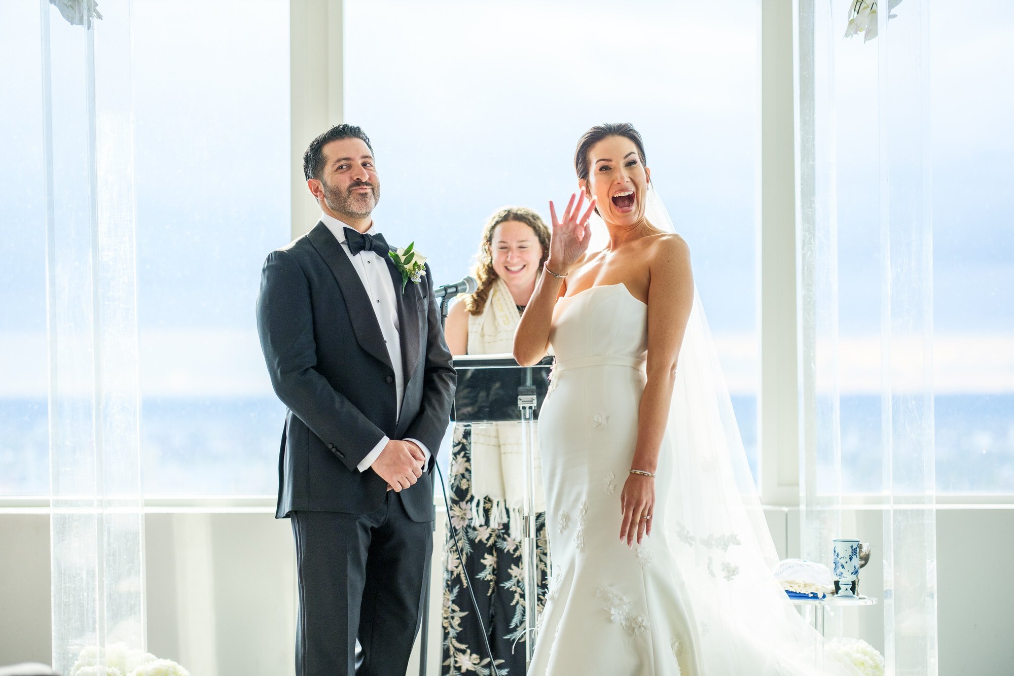 Bride laughing and showing off her new wedding ring to guests during the ceremony at the UMass Club Boston