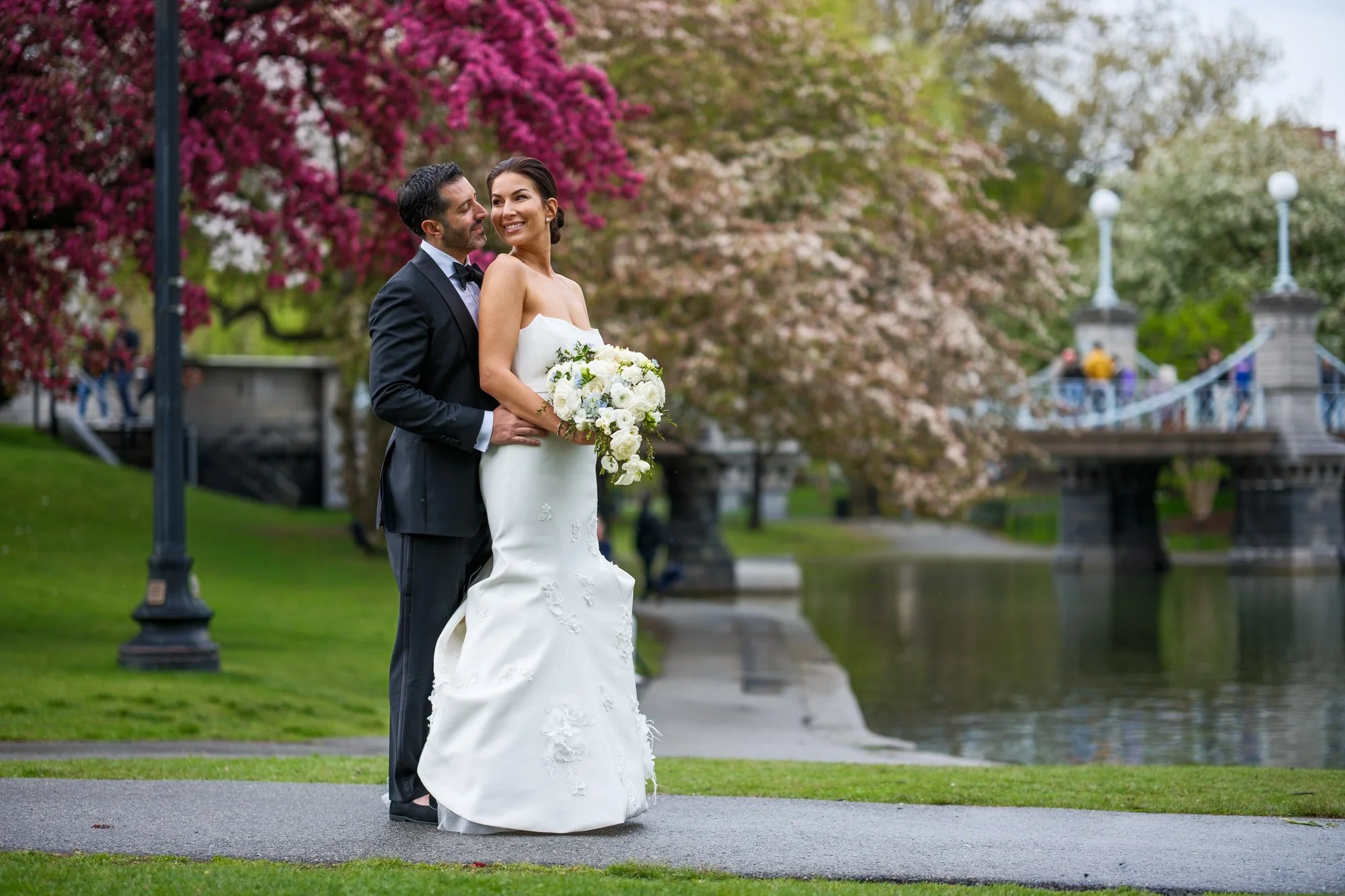 Bride and groom posing near the Boston Public Garden lagoon bridge surrounded by pink blossoms