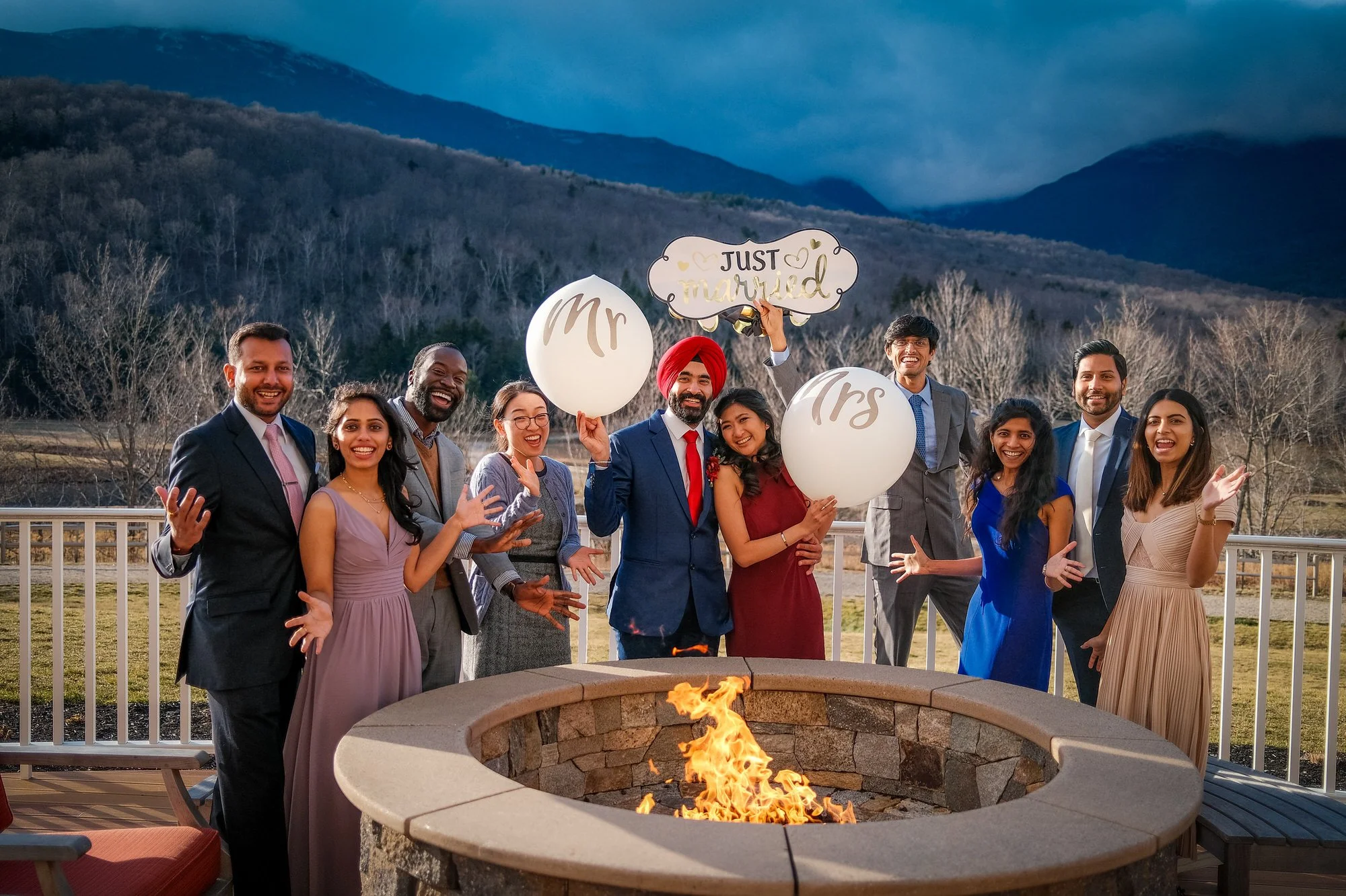 Newlyweds laughing together with friends by a fire with a wooded setting near the Glen House, Mt. Washington, New Hampshire winter elopement