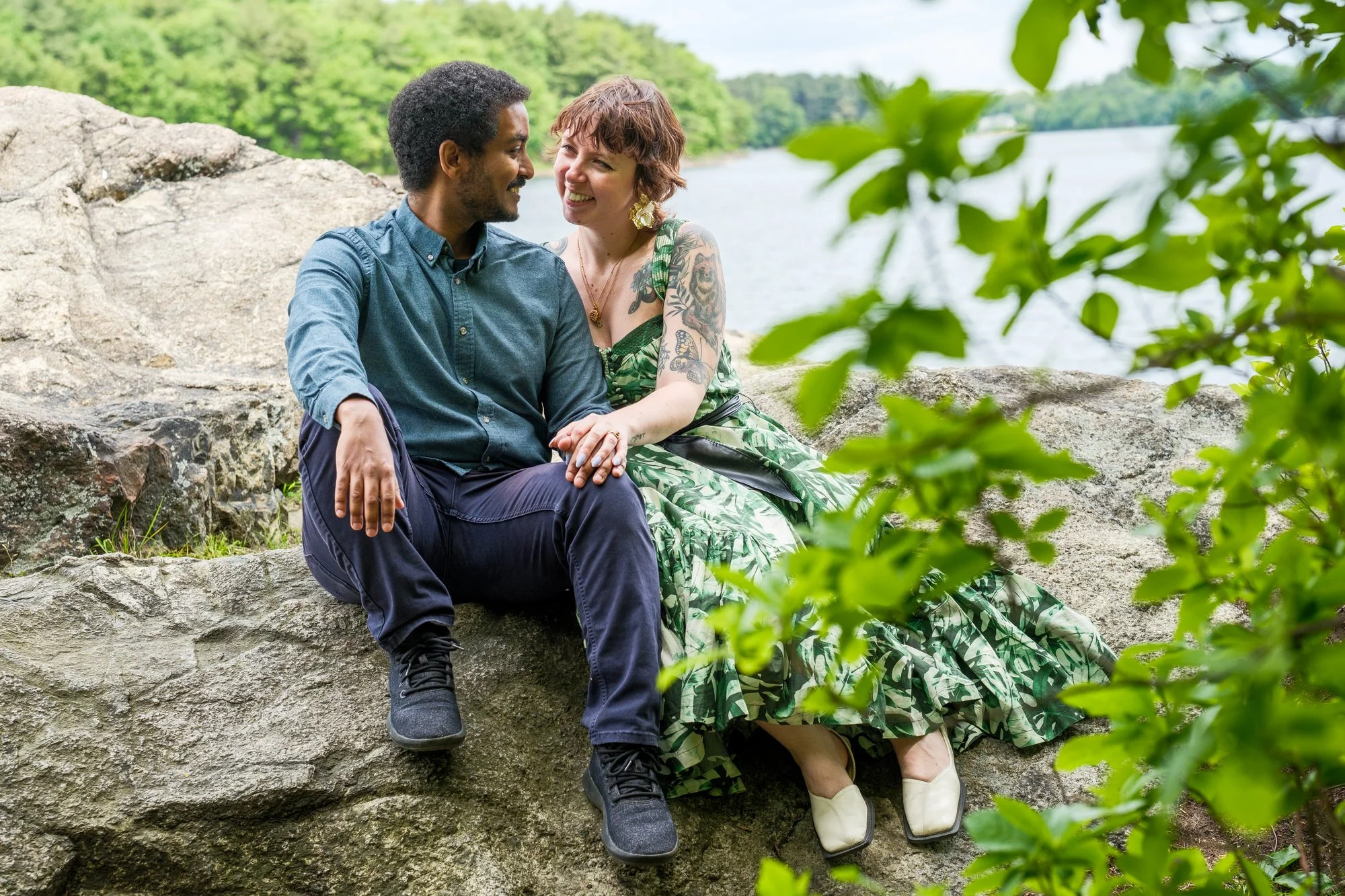 Newly engaged couple sitting together on a rocky overlook at Middlesex Fells Reservation