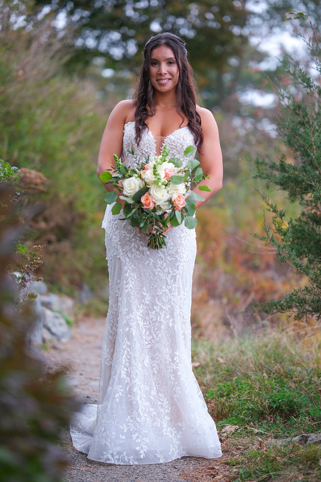Bridal portrait in lace gown holding peach and white bouquet surrounded by autumn foliage in York Maine