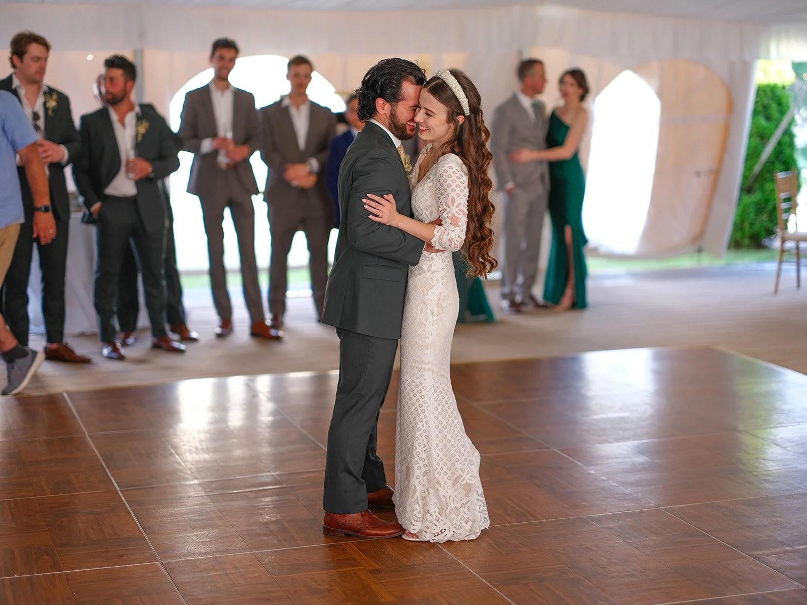 A bride and groom dancing closely during their wedding reception with friends and family in the background inside a tent.