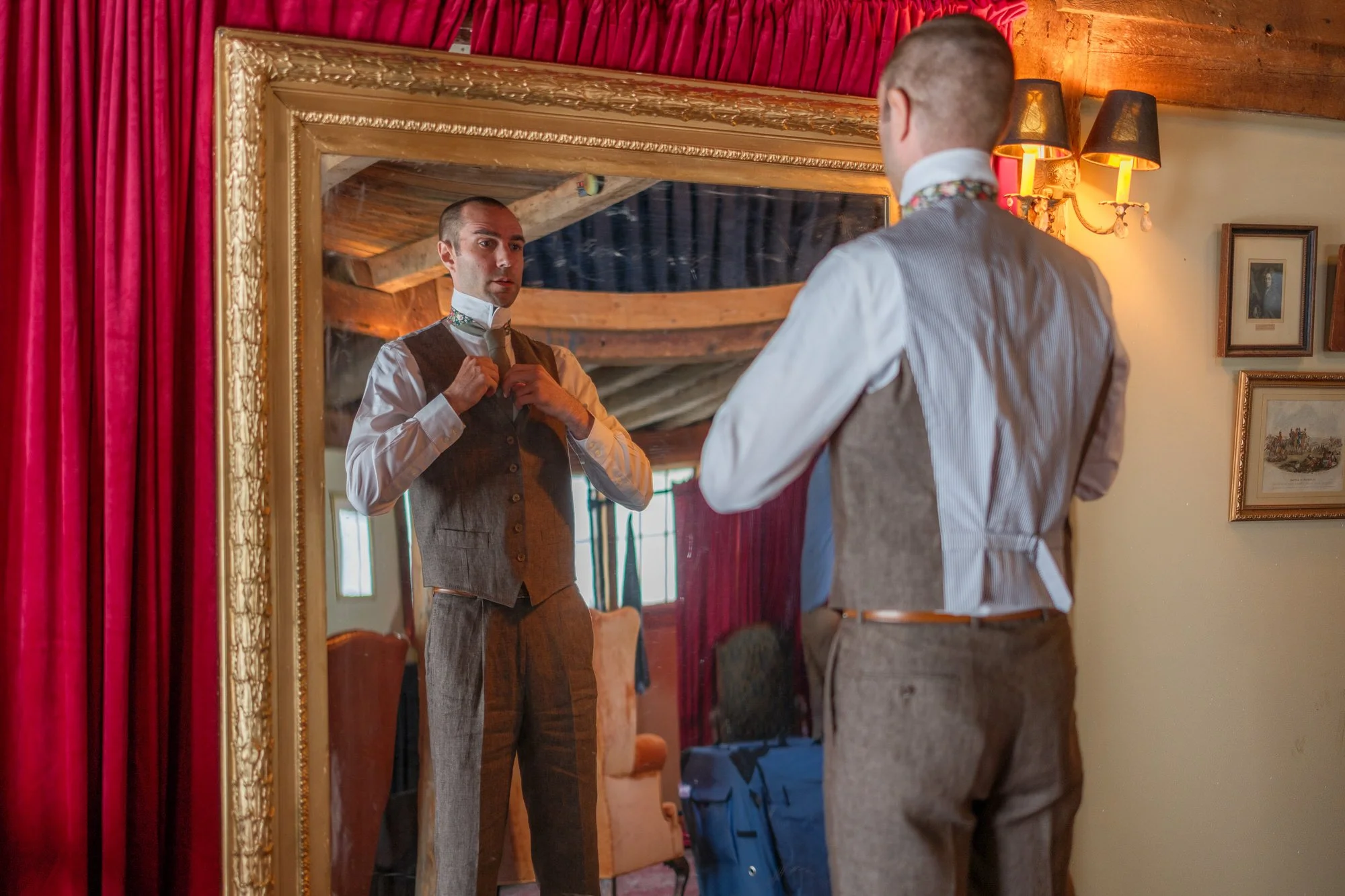 Groom adjusting his tie in an ornate mirror before the wedding
