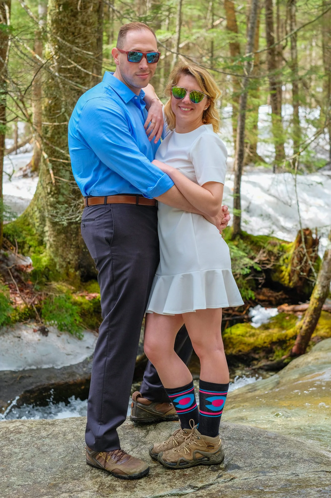 Newlyweds posing together on a mossy rock beside an icy stream in the White Mountains forest during their early spring elopement