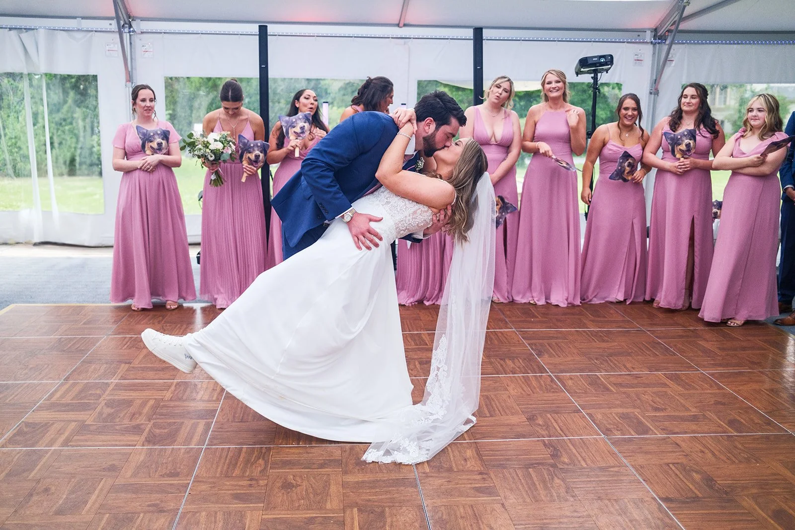 A bride and groom share a kiss on the dance floor during their wedding reception, with bridesmaids in pink dresses standing in the background.