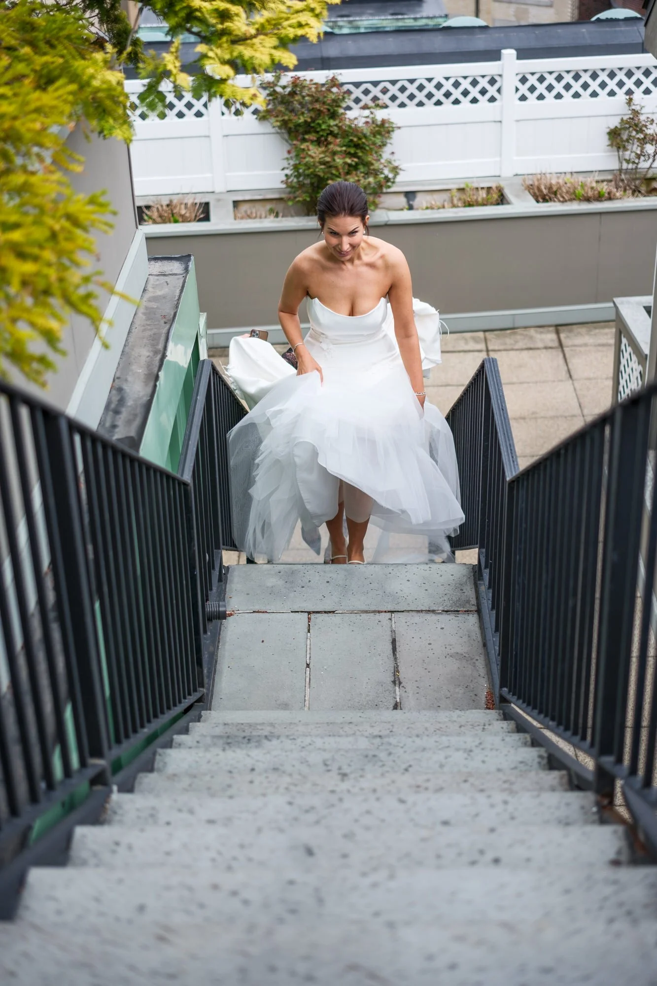 Bride in white strapless gown lifting her dress while climbing outdoor stairs at the XV Beacon Hotel Boston