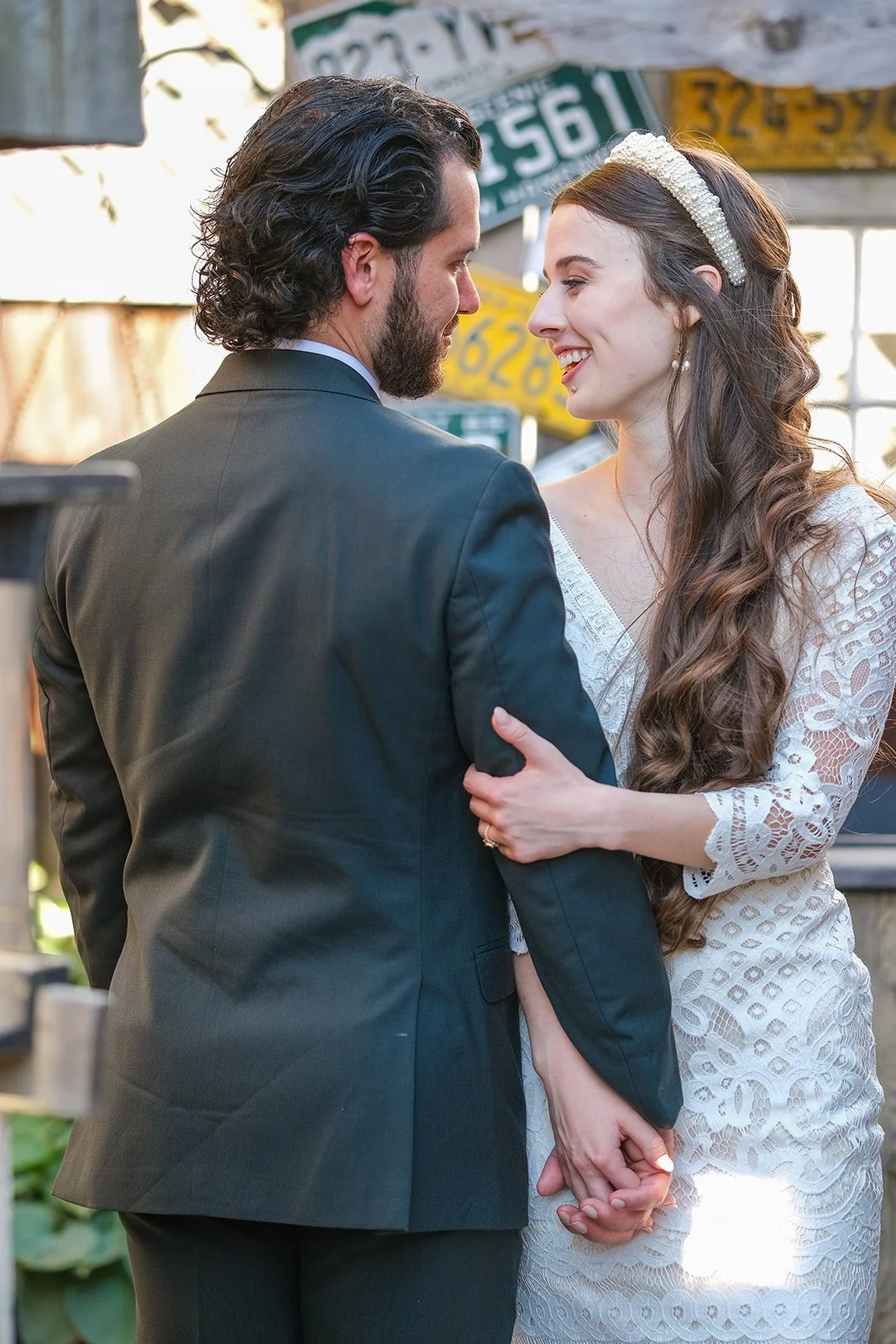 A newly married couple holding hands and gazing into each other's eyes outdoors, with street signs in the background.