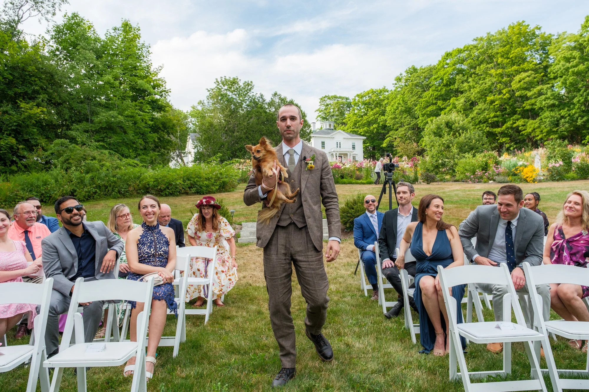 Groom walking down the outdoor ceremony aisle with a small dog