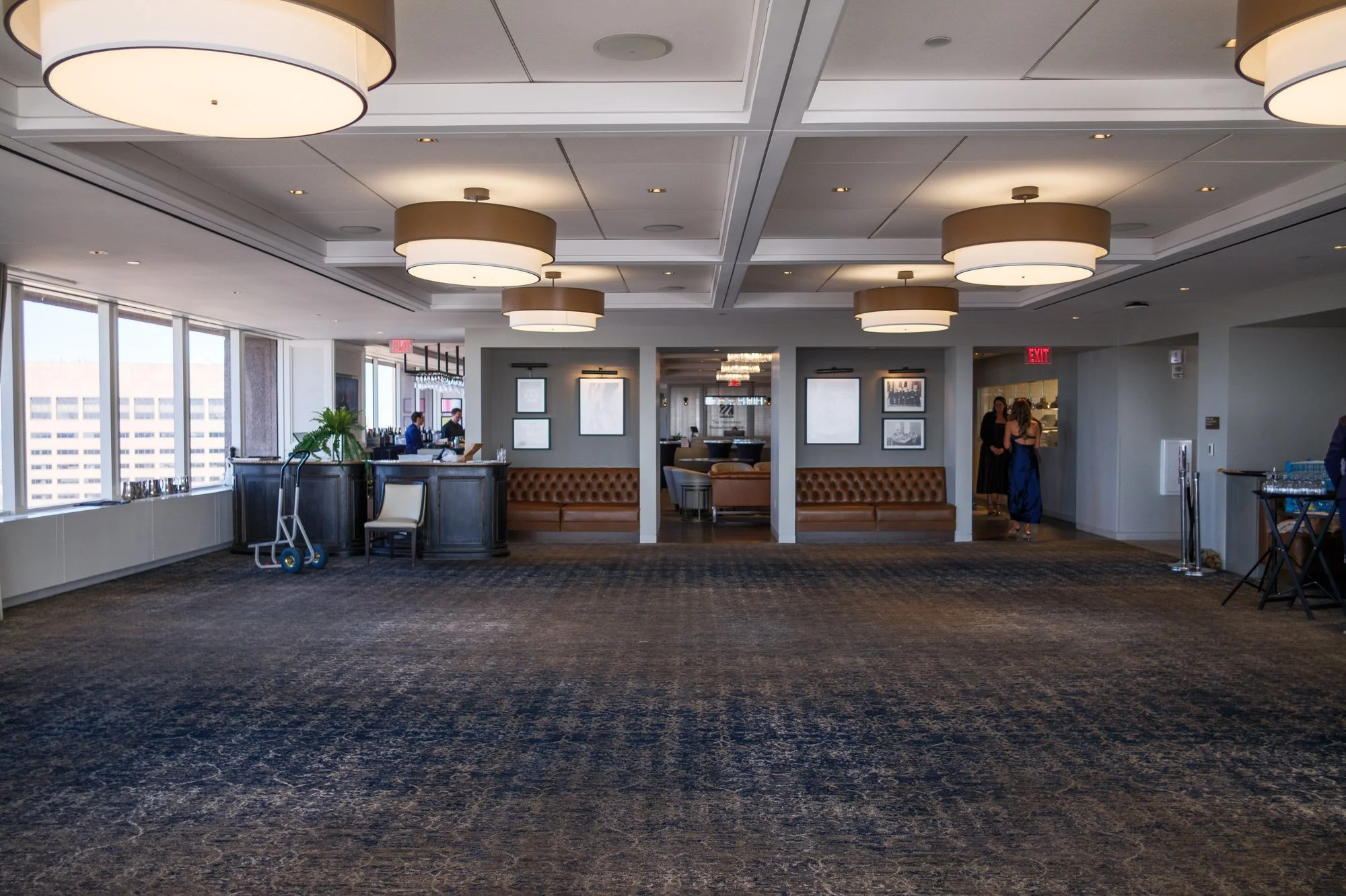 Spacious private event room at the UMass Club in Boston with warm drum pendant lighting, tufted leather banquettes, and city views, set up for Lauren and Charlie's rehearsal dinner