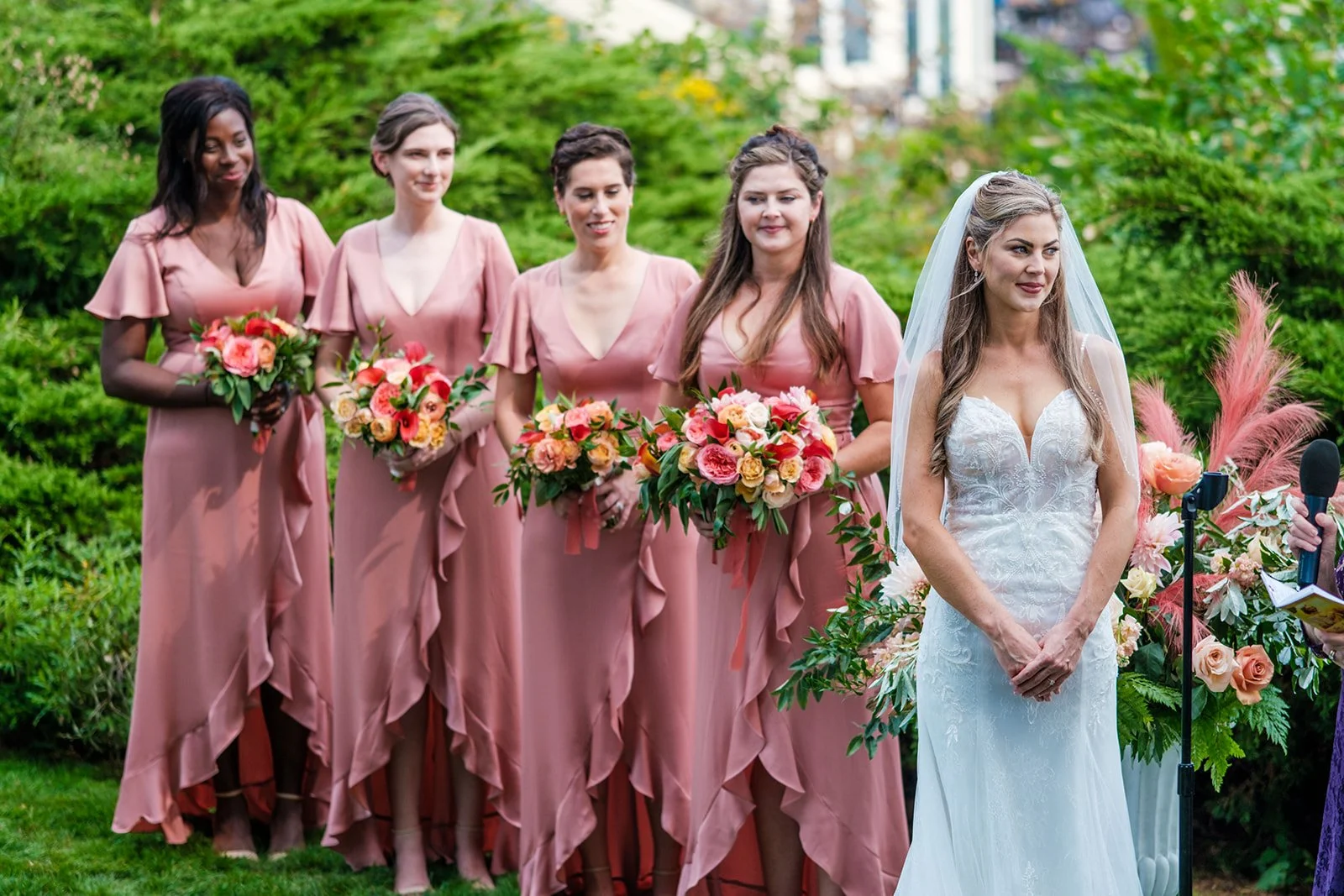 Bride with bridesmaids in dusty rose gowns holding coral bouquets during outdoor ceremony in York Maine