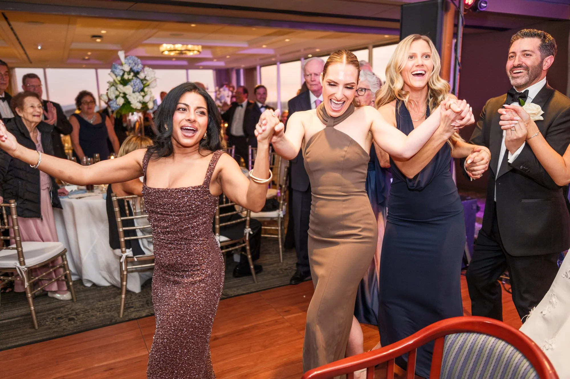 Guests dancing exuberantly during the hora at the UMass Club Boston Jewish wedding reception with groom visible