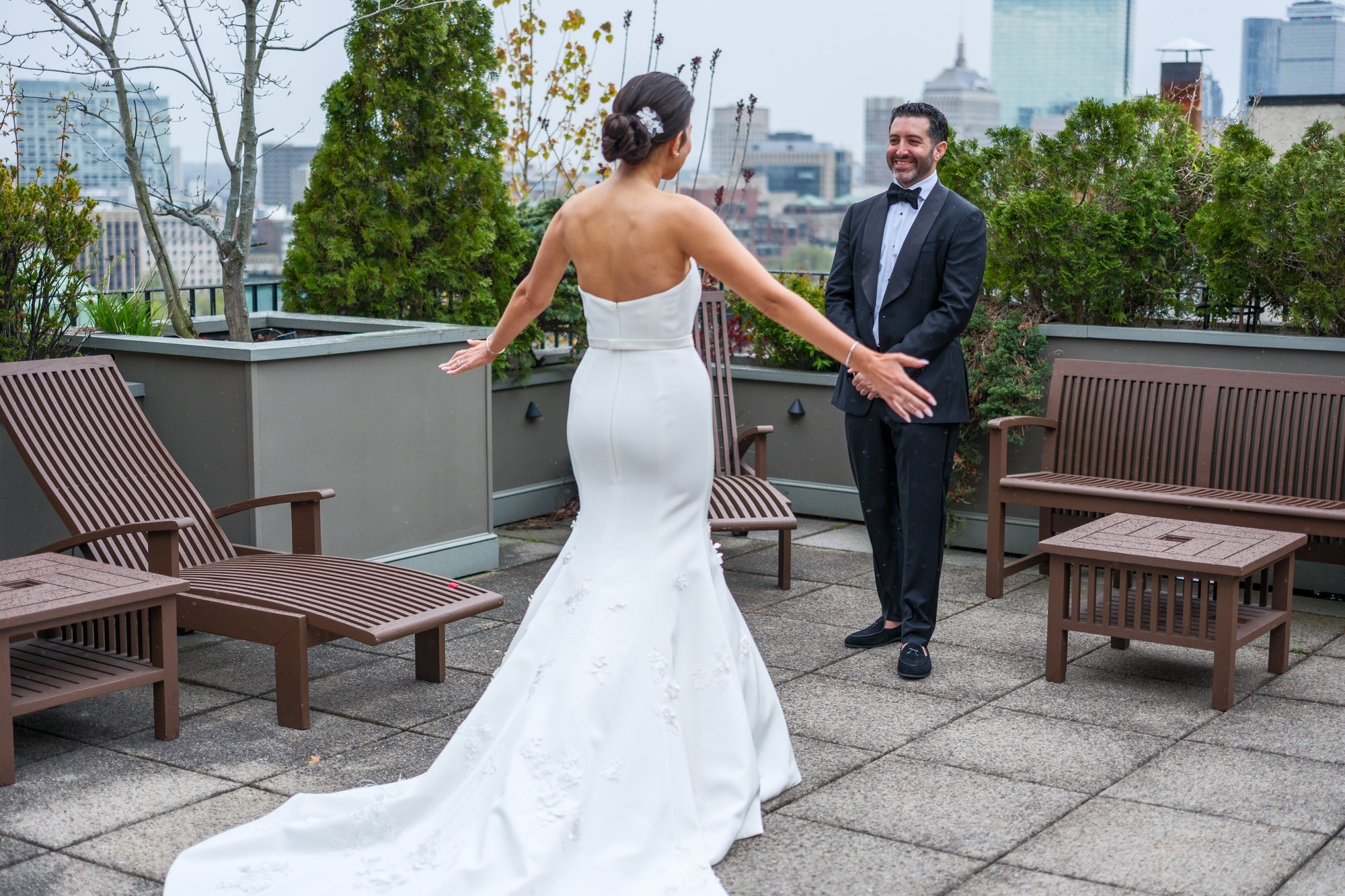 Groom reacting with joy during first look with bride on the XV Beacon Hotel rooftop terrace with Boston skyline