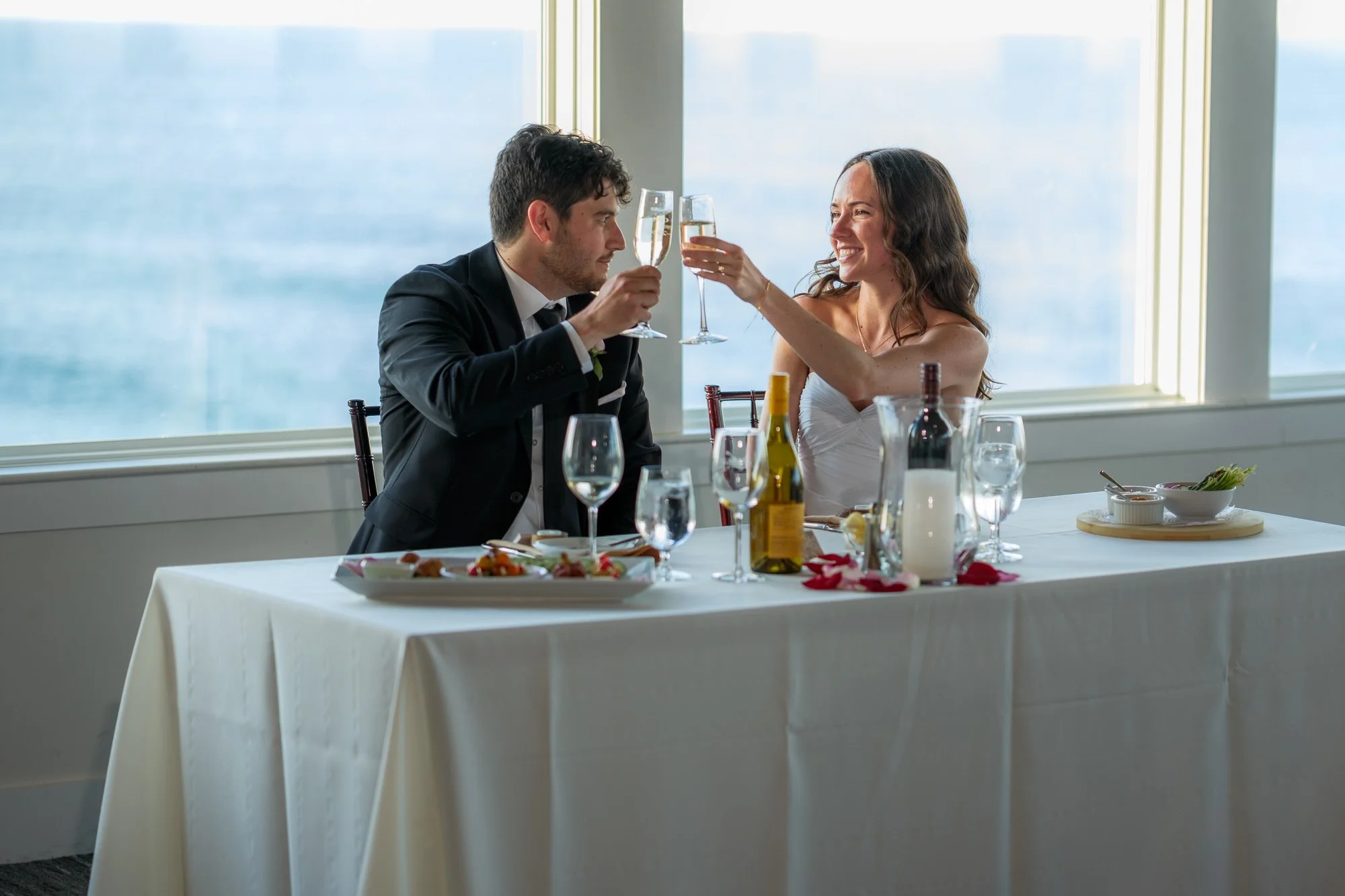 Bride and groom clinking glasses at their ocean-view reception at Blue Ocean Event Center.