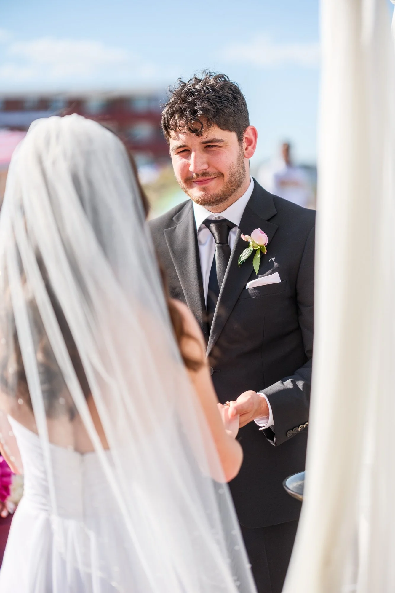 Groom listening during vows at a sunny Blue Ocean Event Center beach wedding ceremony.