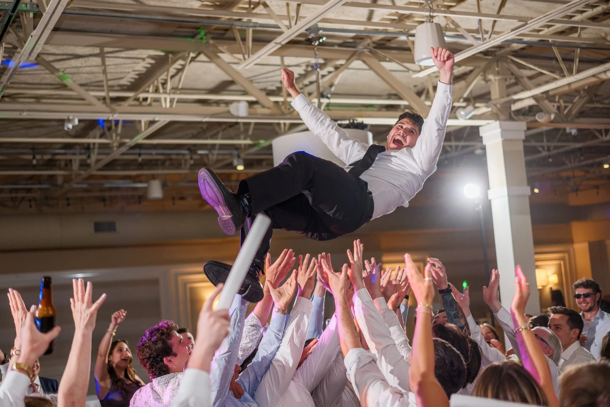 Groom lifted in a chair above cheering wedding guests at Blue Ocean Event Center.