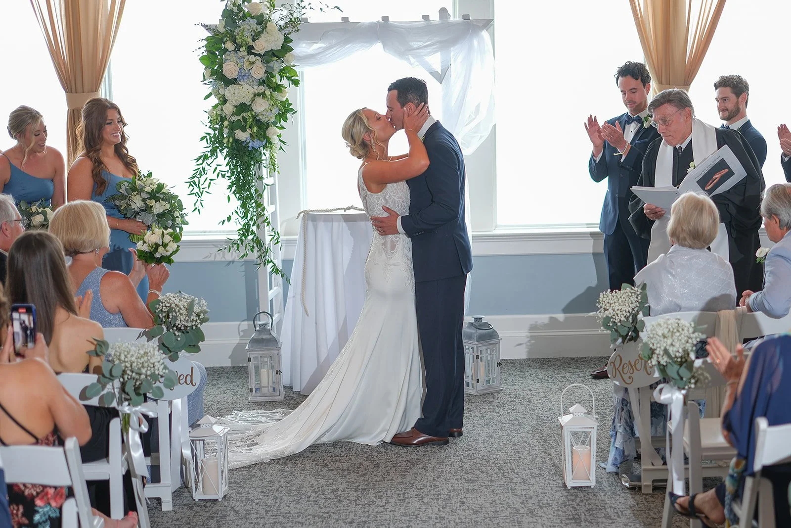 Couple's first kiss during indoor wedding ceremony at Blue Ocean Event Center in Salisbury MA with bridal party cheering