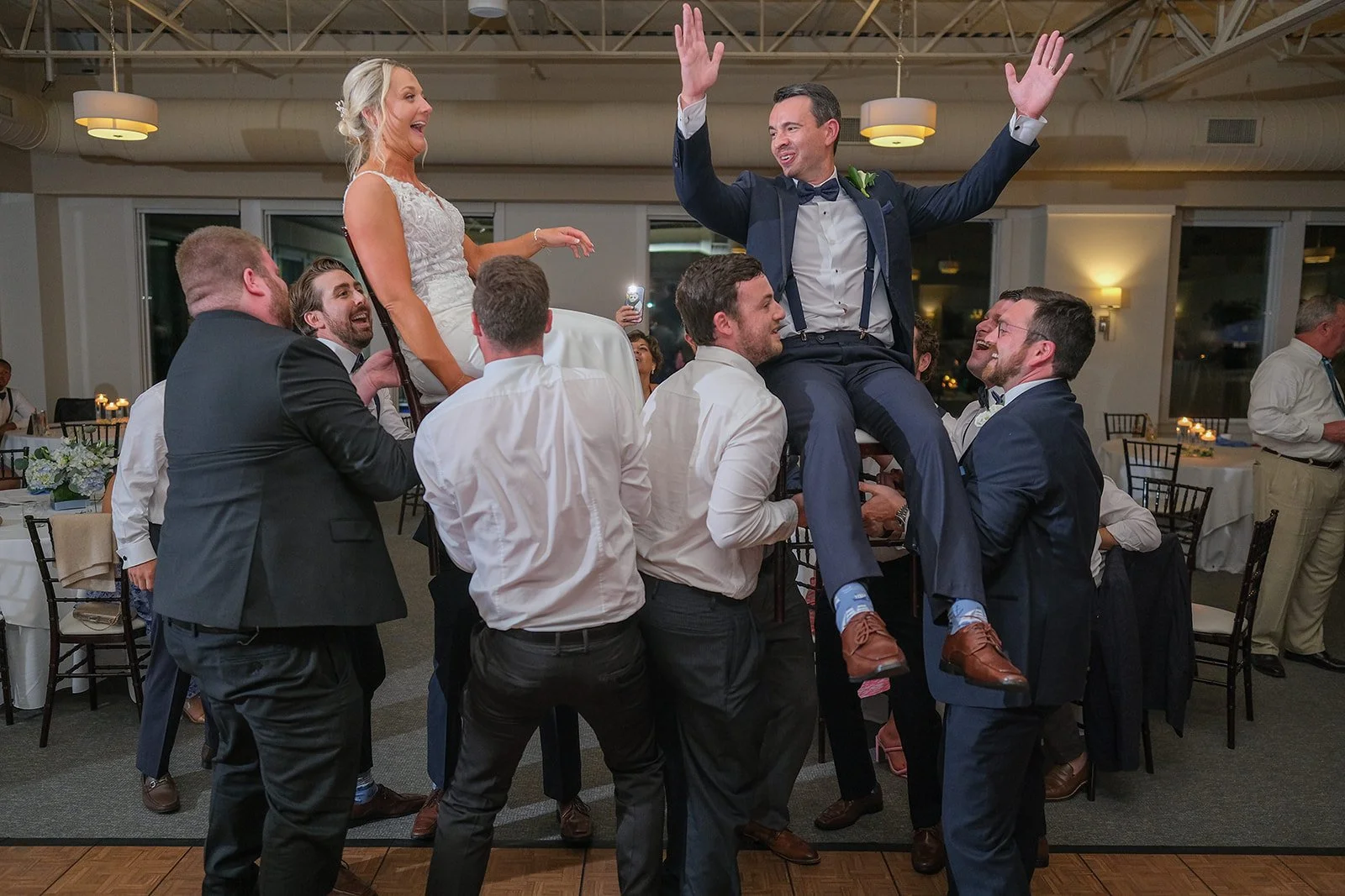 Bride and groom both lifted by guests during joyful wedding reception celebration at Blue Ocean Event Center Salisbury MA