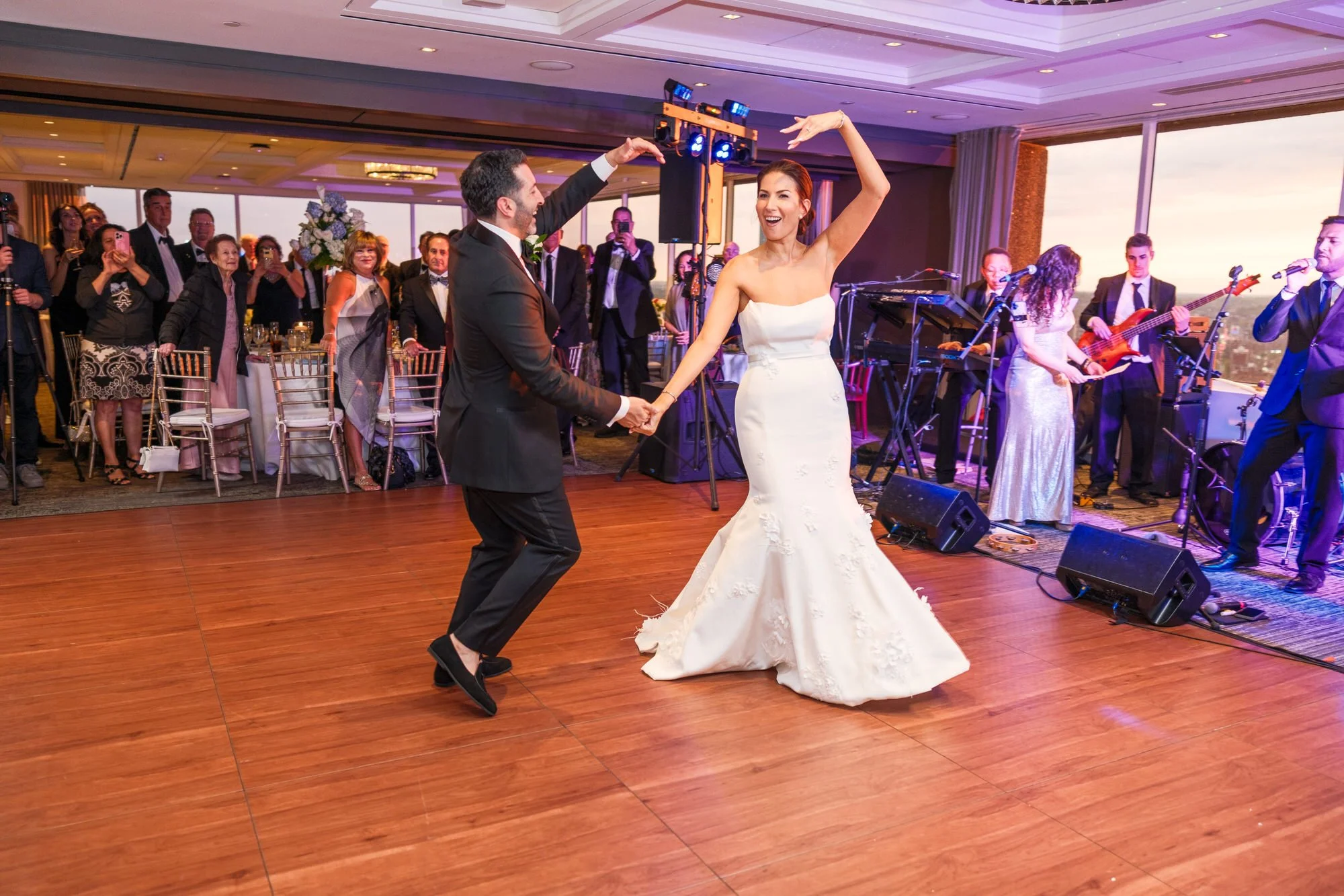 Groom twirling bride during energetic first dance at the UMass Club Boston with live band and cheering guests