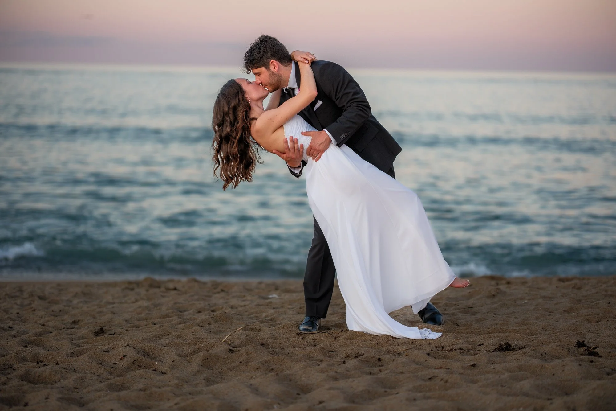 Groom dipping the bride for a romantic kiss on the beach near Blue Ocean Event Center.