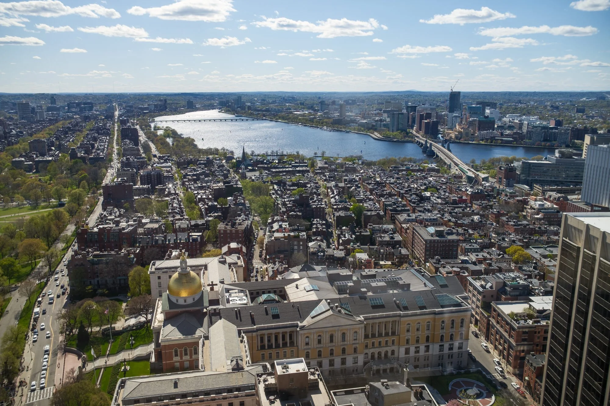 Aerial view of Boston skyline and Charles River from the UMass Club atop the John Hancock Tower, with the Massachusetts State House gold dome in the foreground, captured during Lauren and Charlie's rehearsal dinner weekend