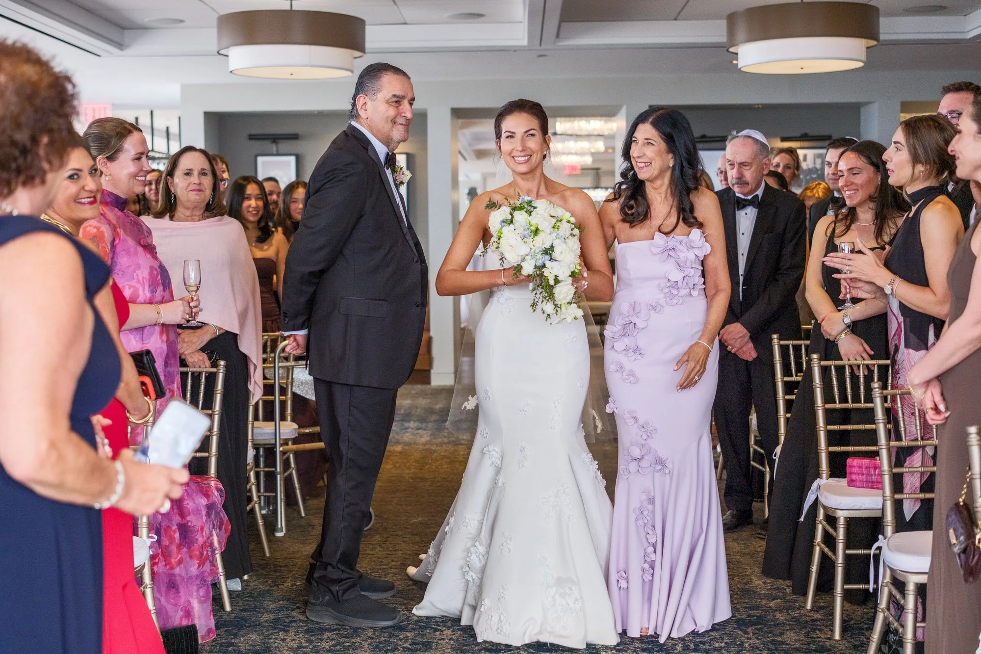 Bride walking down the aisle flanked by her parents during the Jewish wedding ceremony at the UMass Club Boston