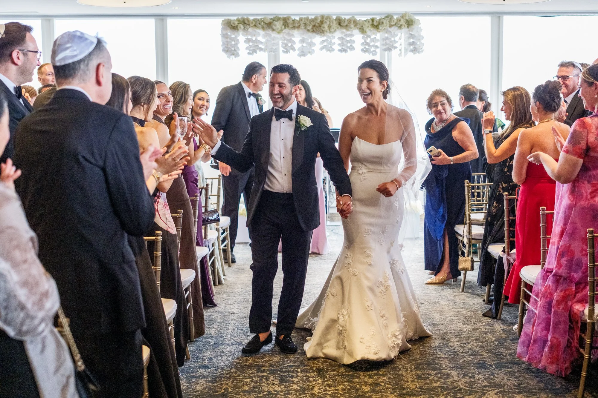 Newlyweds joyfully walking back down the aisle during the recessional at the UMass Club Boston Jewish wedding