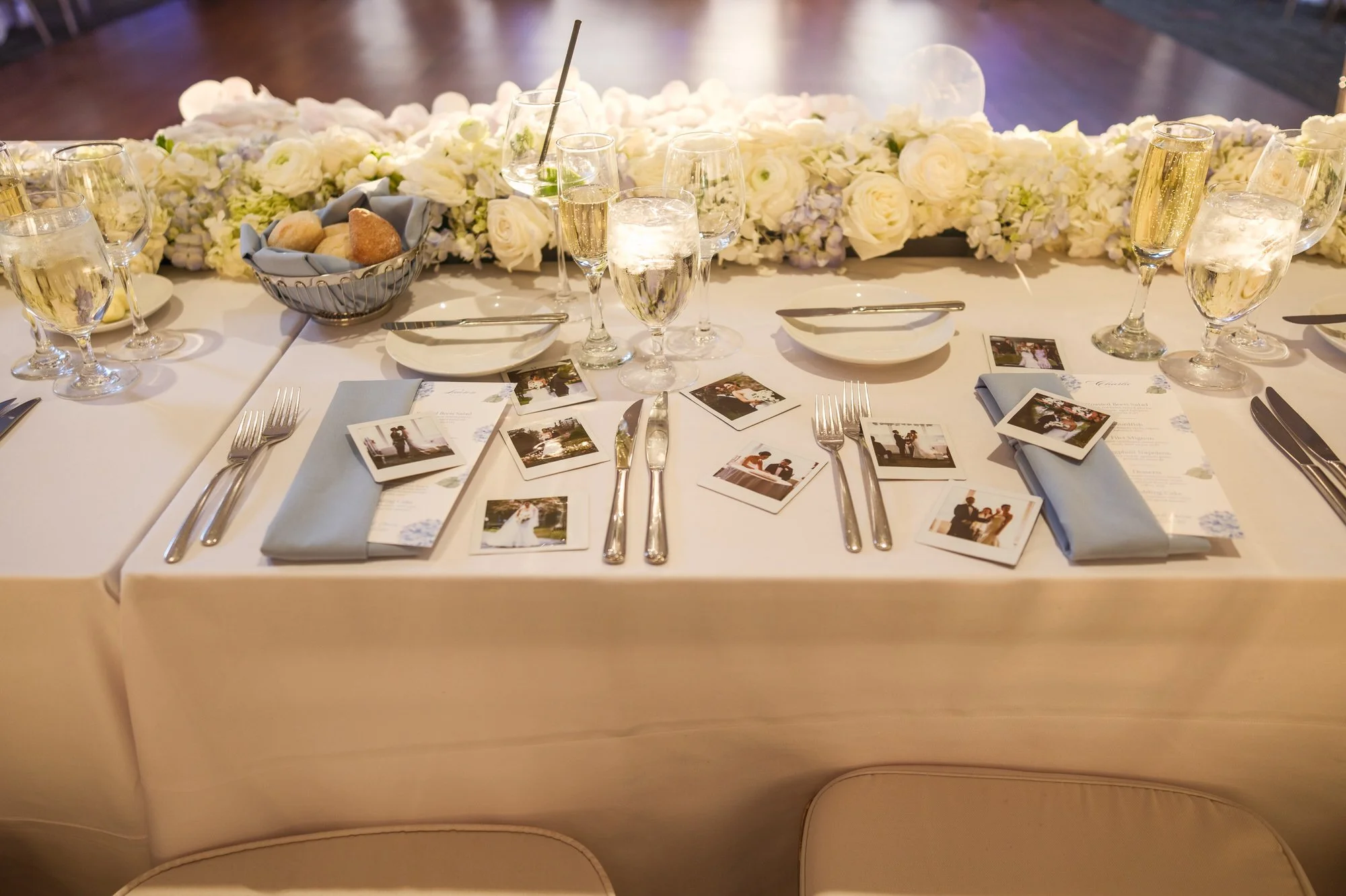 Elegant UMass Club Boston wedding reception table featuring polaroid photo favors, blue napkins, and white floral runner