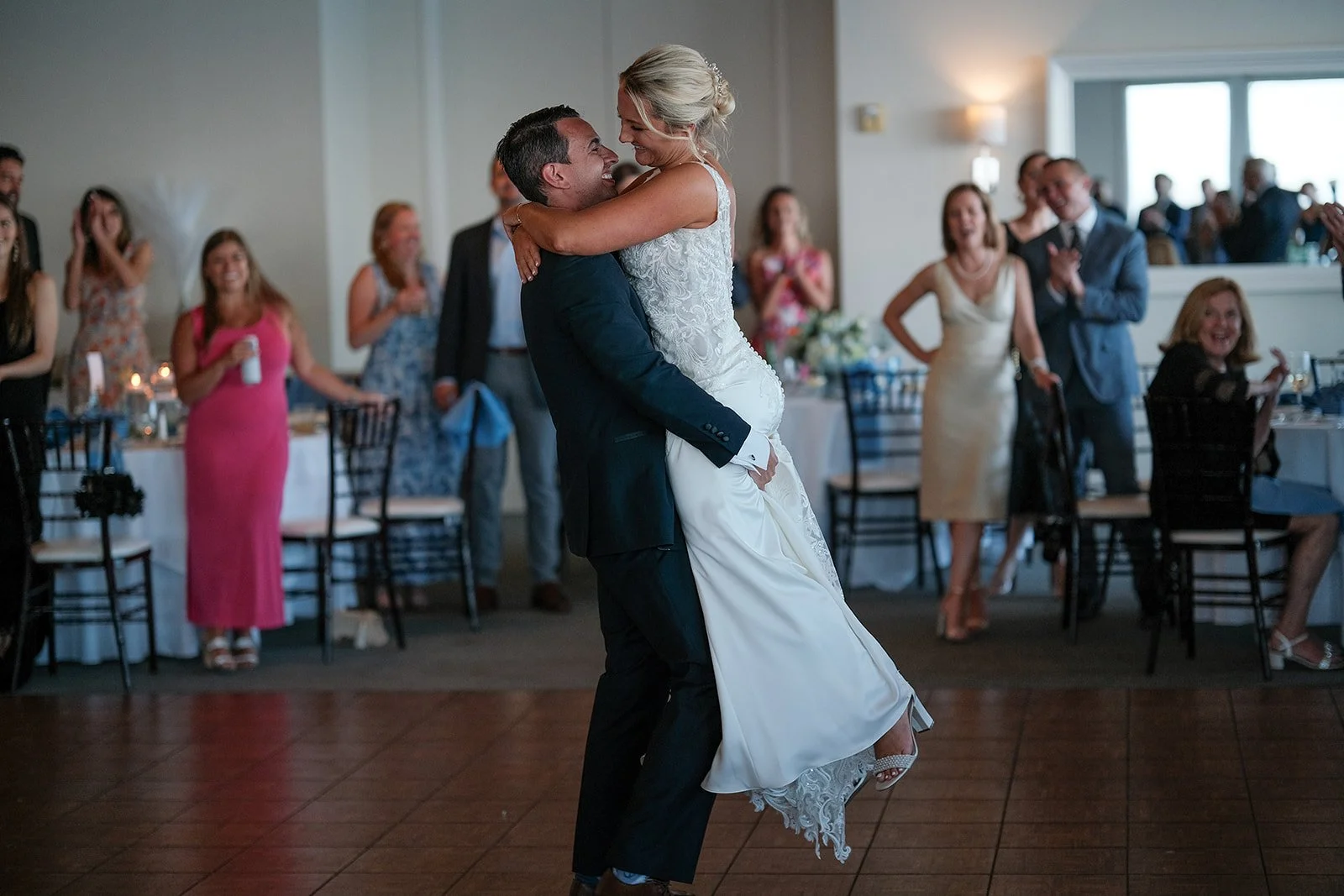 Groom lifting bride off the ground during first dance at Blue Ocean Event Center reception with guests cheering